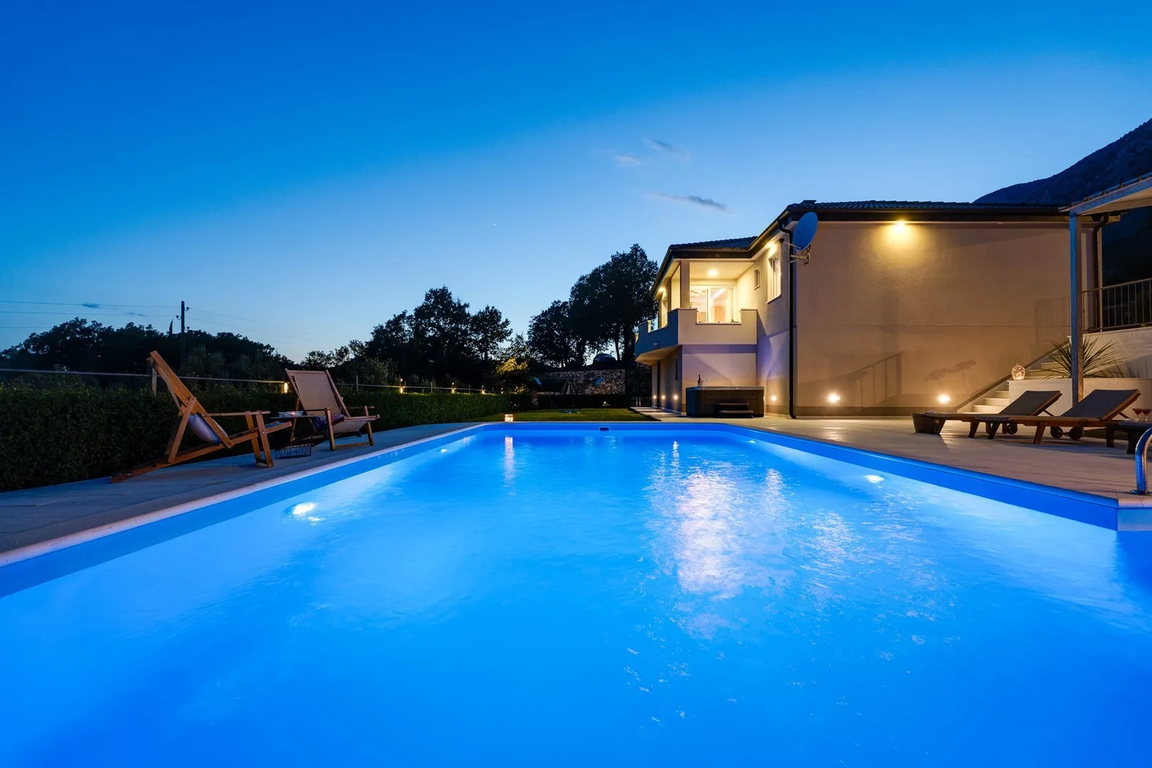 An illuminated swimming pool beside a modern building at dusk.