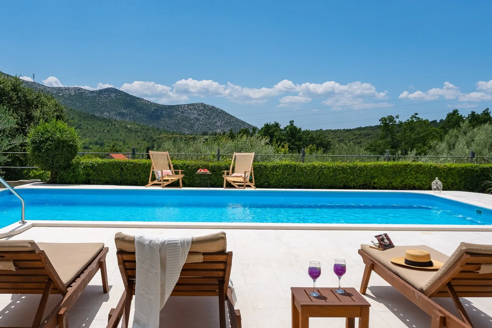 An outdoor swimming pool beside sun loungers, with green hills in the background.