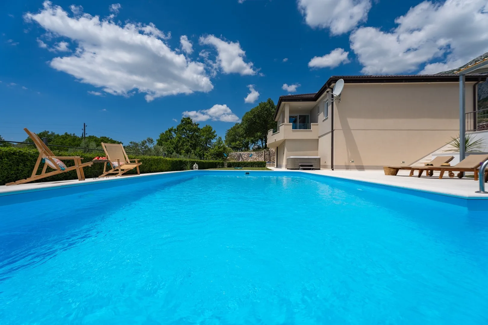 An outdoor swimming pool beside a house, with loungers around the pool.