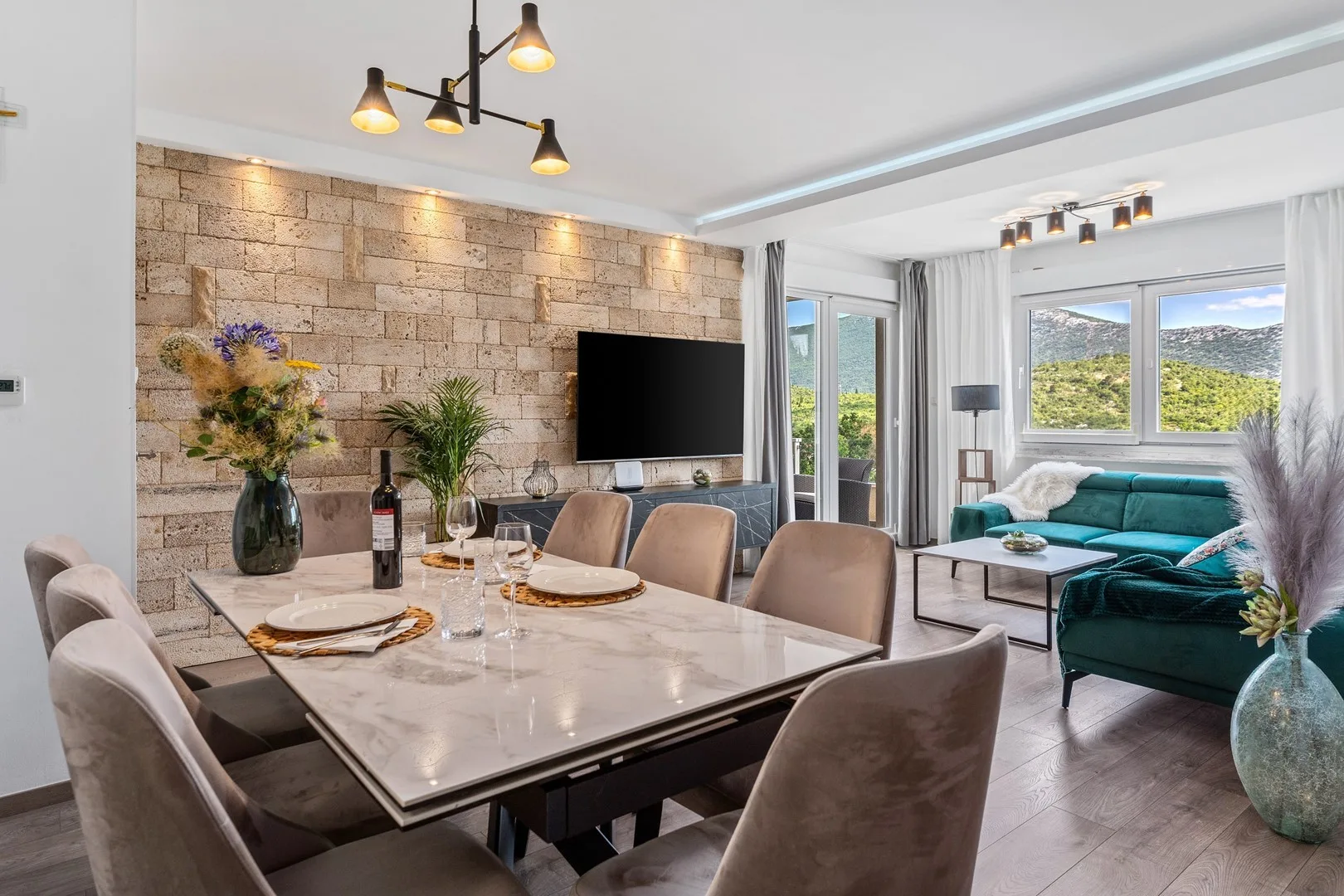 A dining area opens into a living room with a teal sectional and large windows.