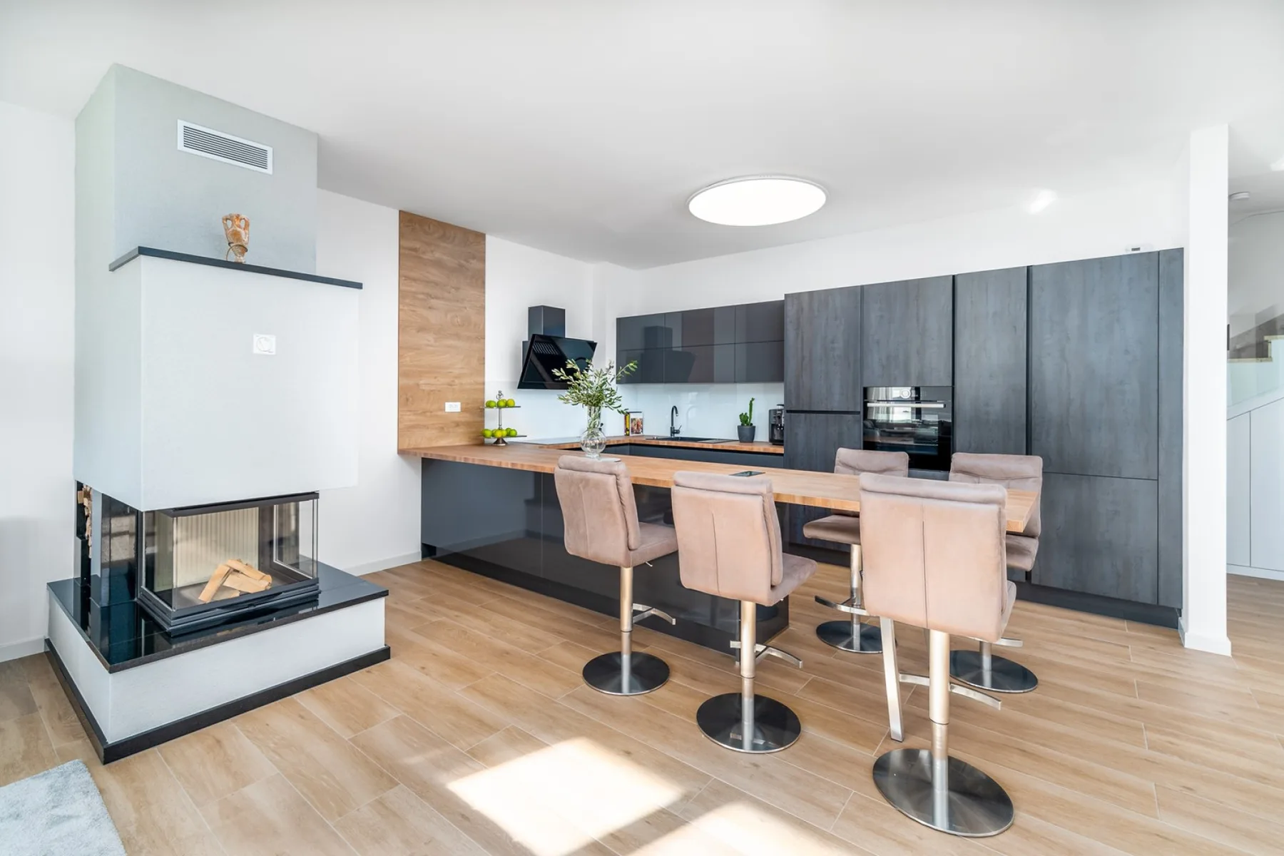 Modern kitchen with dark cabinets, a wood-topped island, upholstered bar stools, and a glass-front fireplace.