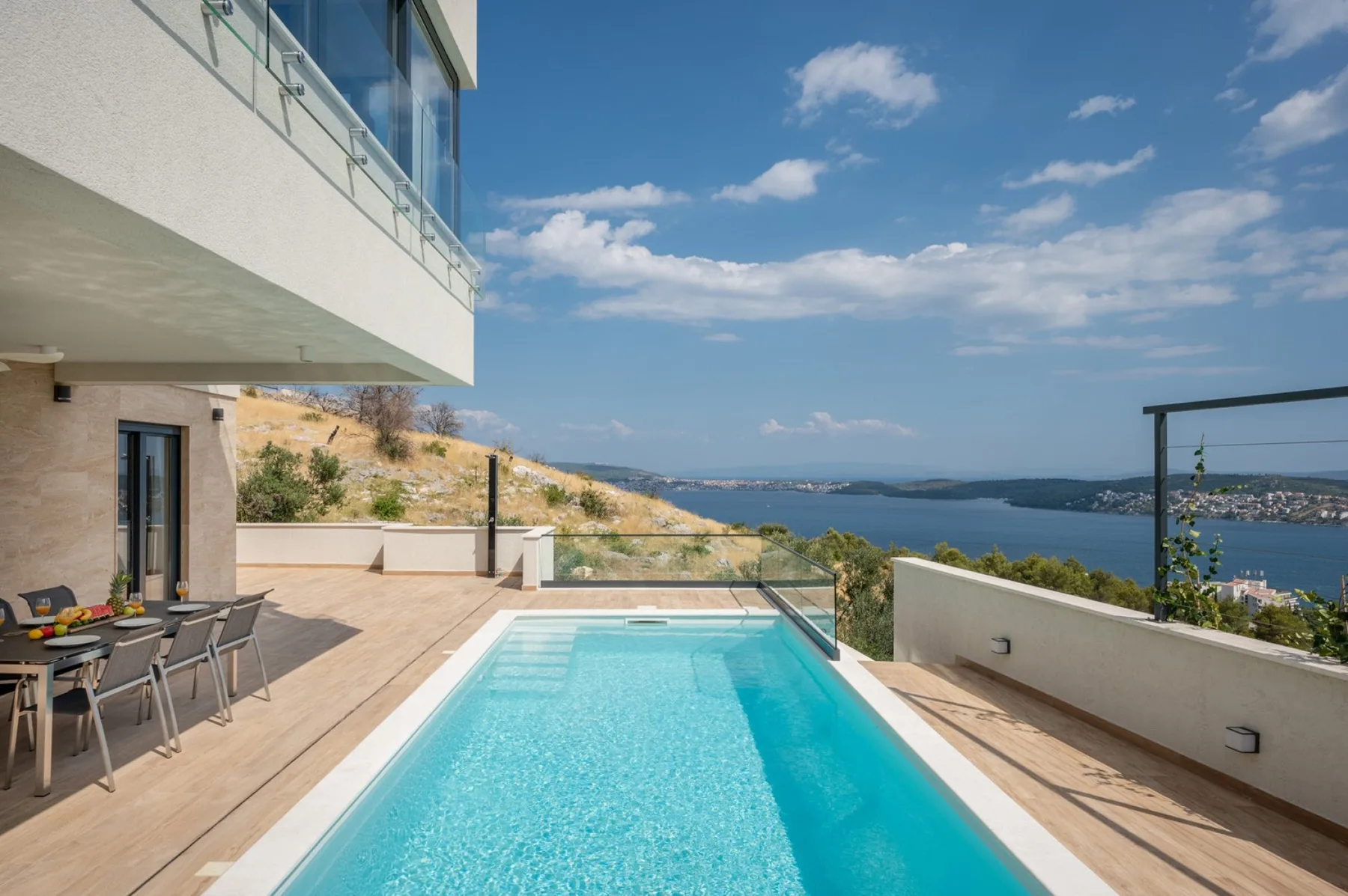 A modern terrace features a rectangular swimming pool, outdoor dining area, and views of the sea.