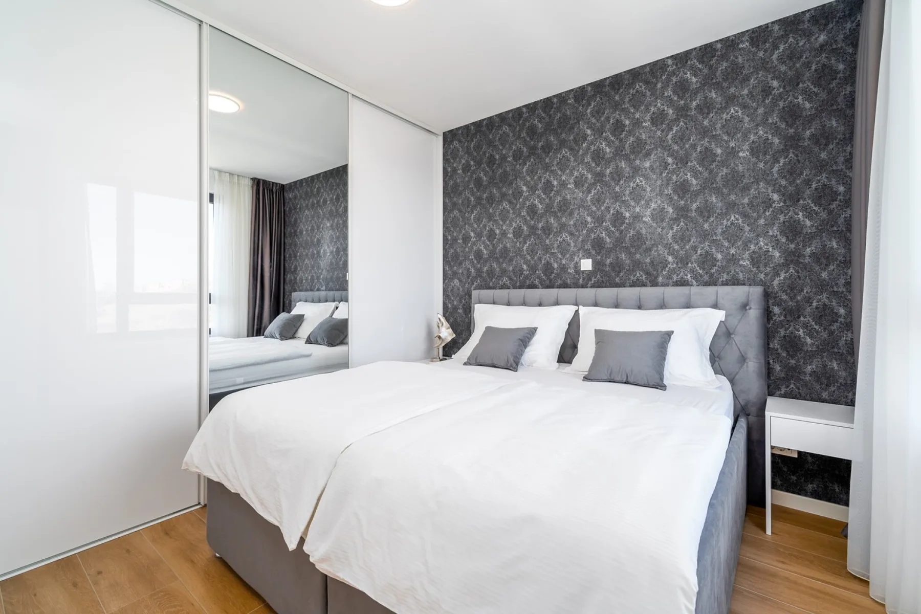 A bedroom with a double bed, mirrored wardrobe doors, and a dark patterned accent wall.