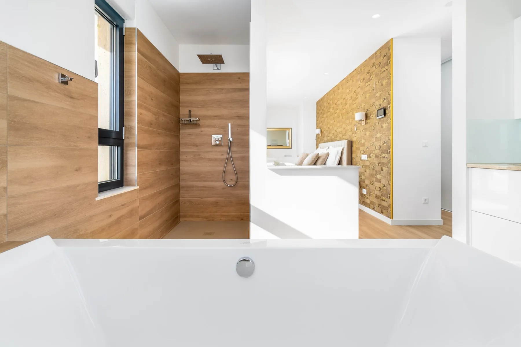 A modern bathroom features a white bathtub, wood-paneled shower, and a view into the adjoining bedroom.