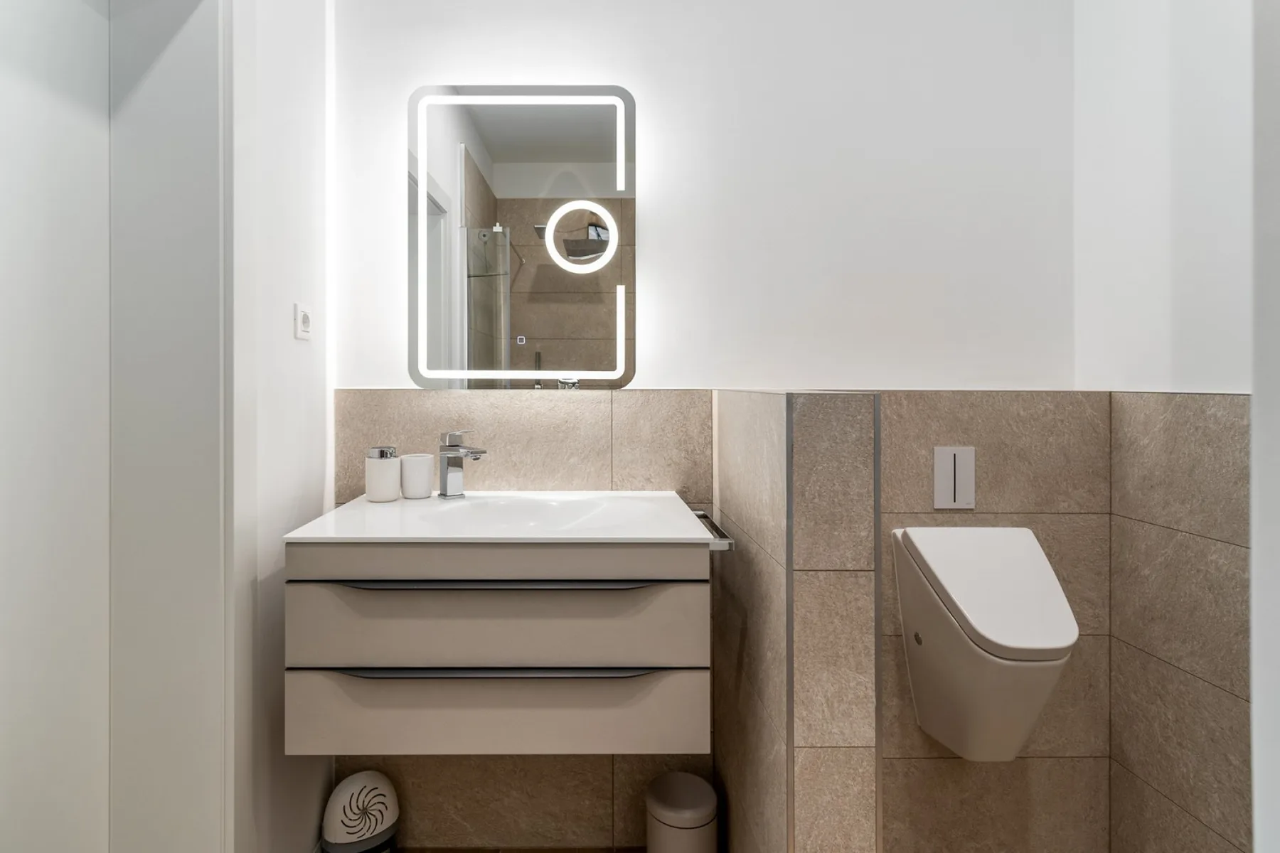 A modern bathroom with a floating vanity, illuminated mirror, and wall-mounted toilet.