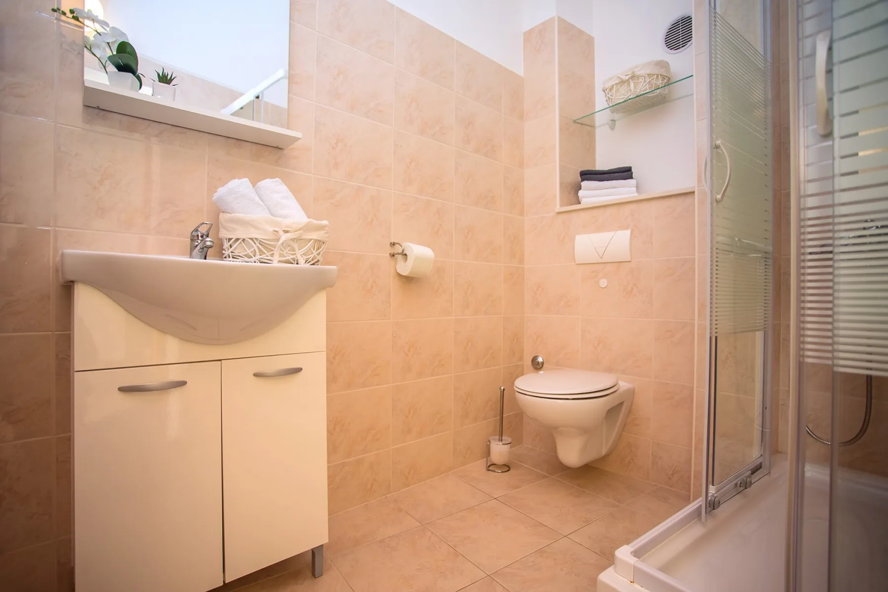 Un baño alicatado con lavabo, inodoro suspendido y ducha de vidrio.