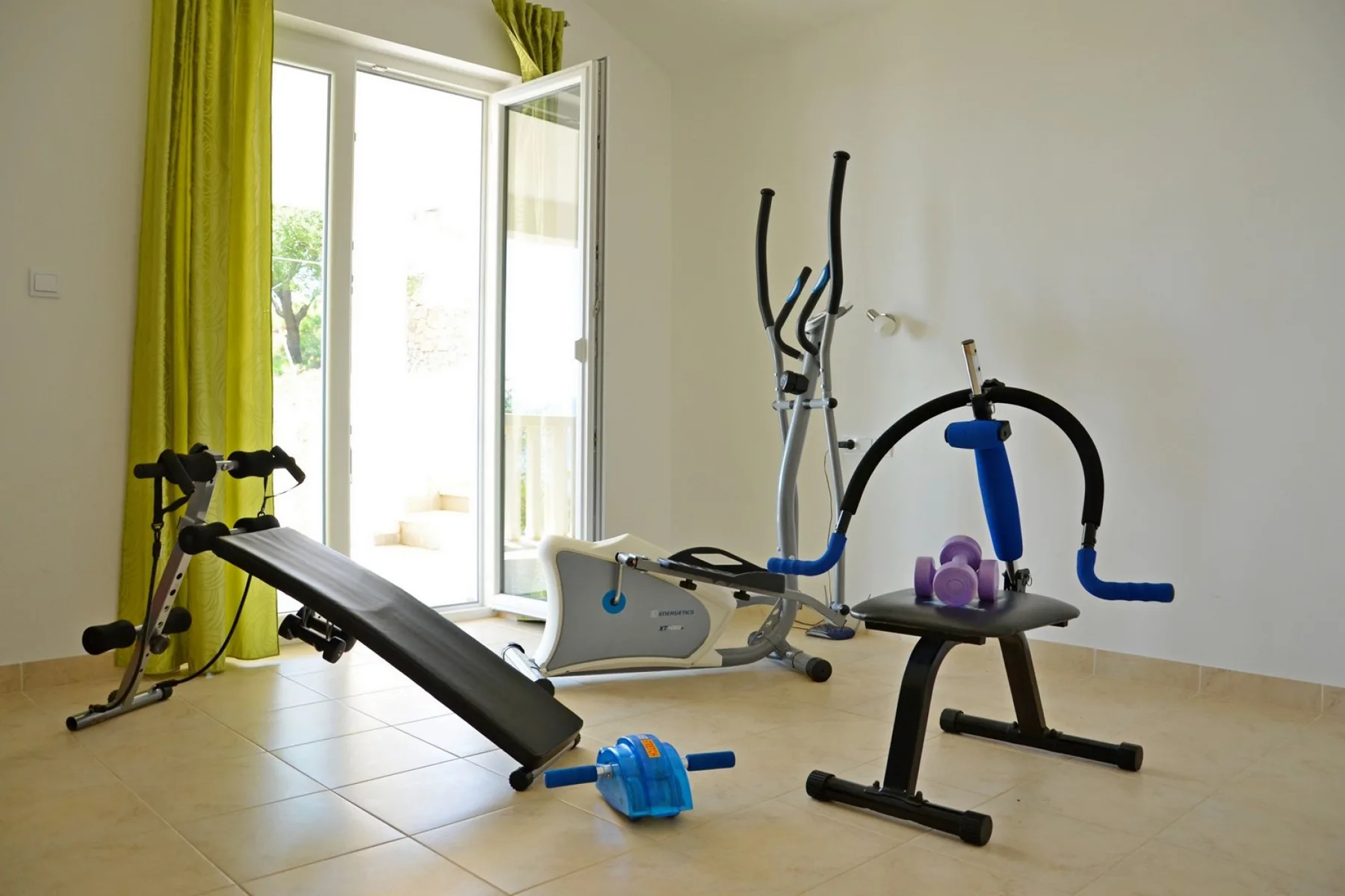 Un gimnasio en casa con equipo de ejercicio junto a una ventana abierta e iluminada.