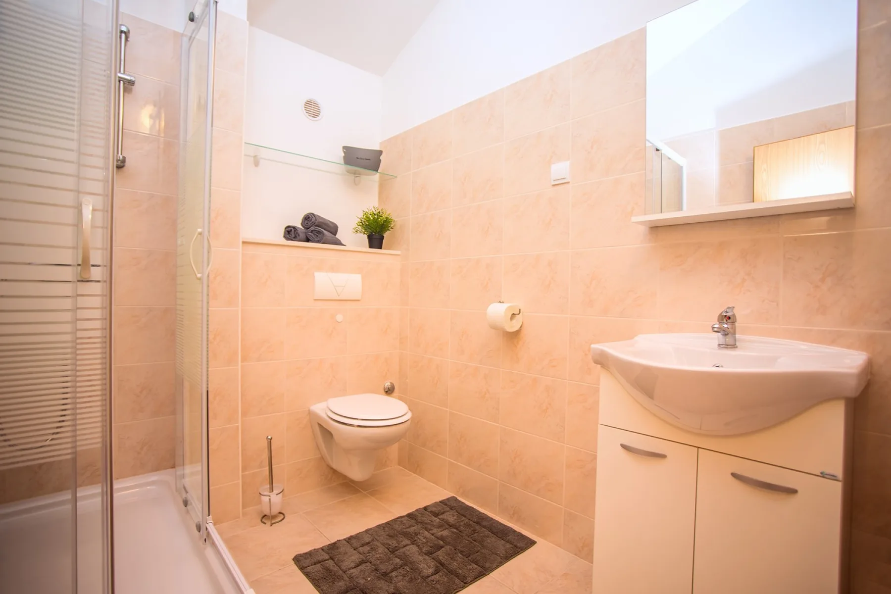 Un baño con azulejos, ducha, inodoro suspendido y lavabo.