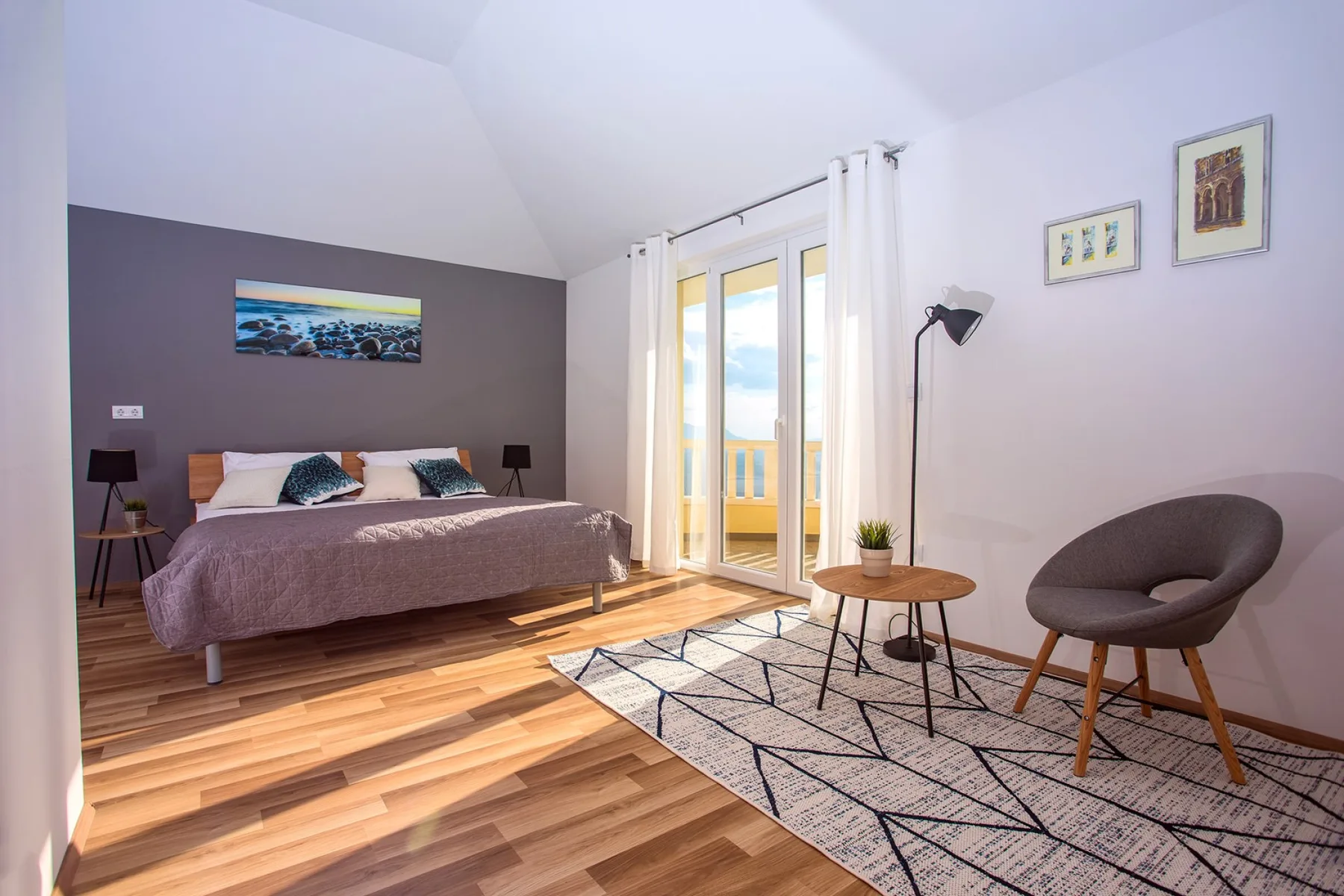 Un dormitorio luminoso con cama, puertas al balcón y una zona de estar.