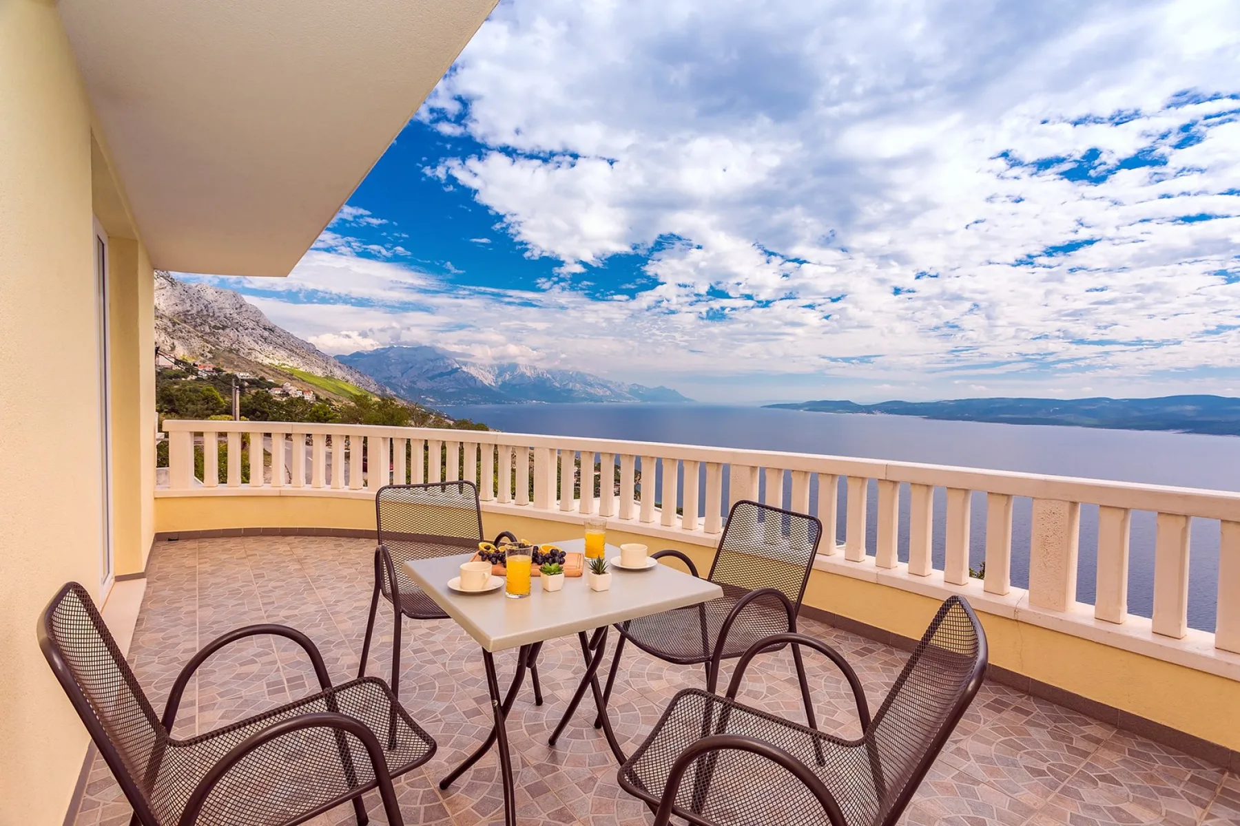 Una terraza con asientos y una mesa al aire libre da al mar y a montañas lejanas.