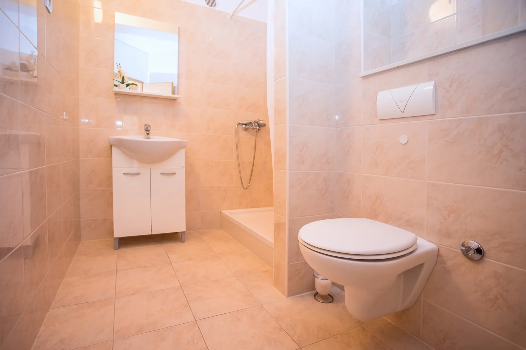 Un baño alicatado con lavabo, ducha e inodoro suspendido.