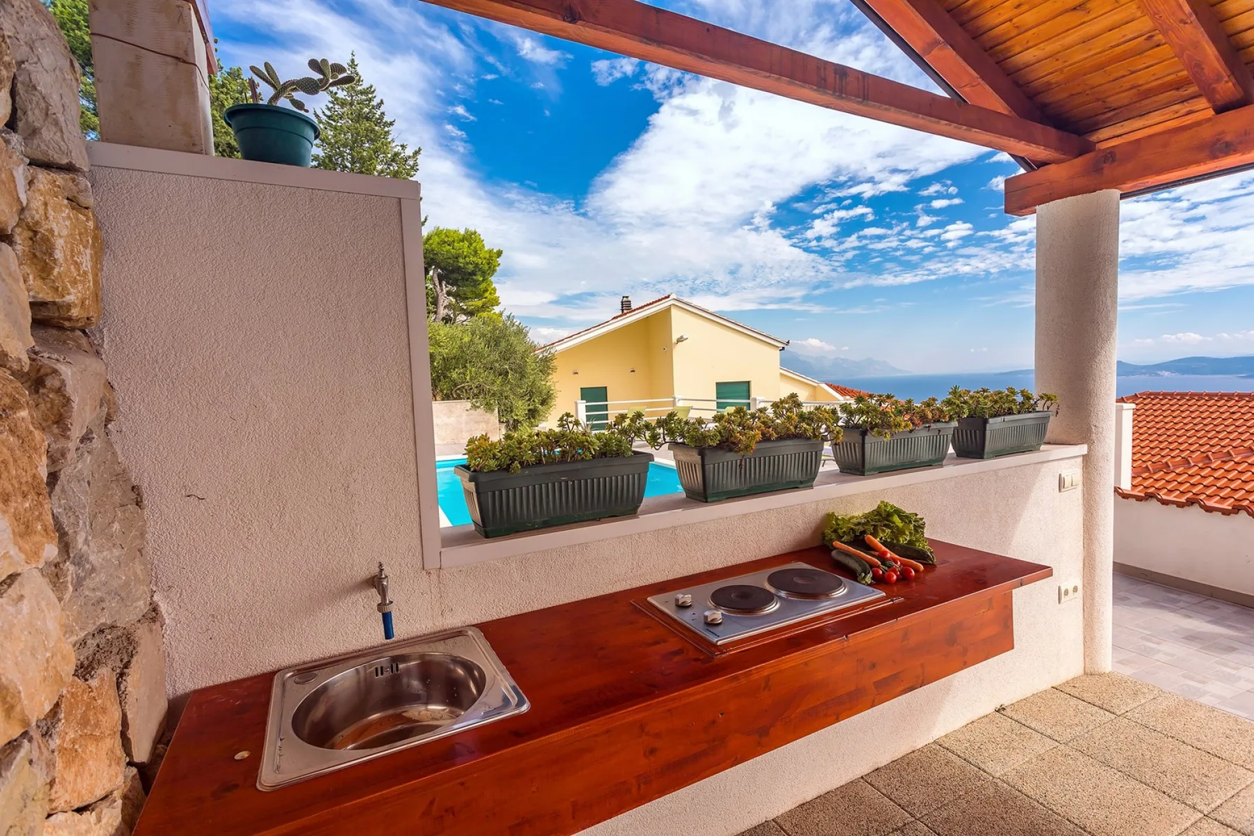 Una encimera de cocina exterior da a una piscina, casas cercanas y el mar.