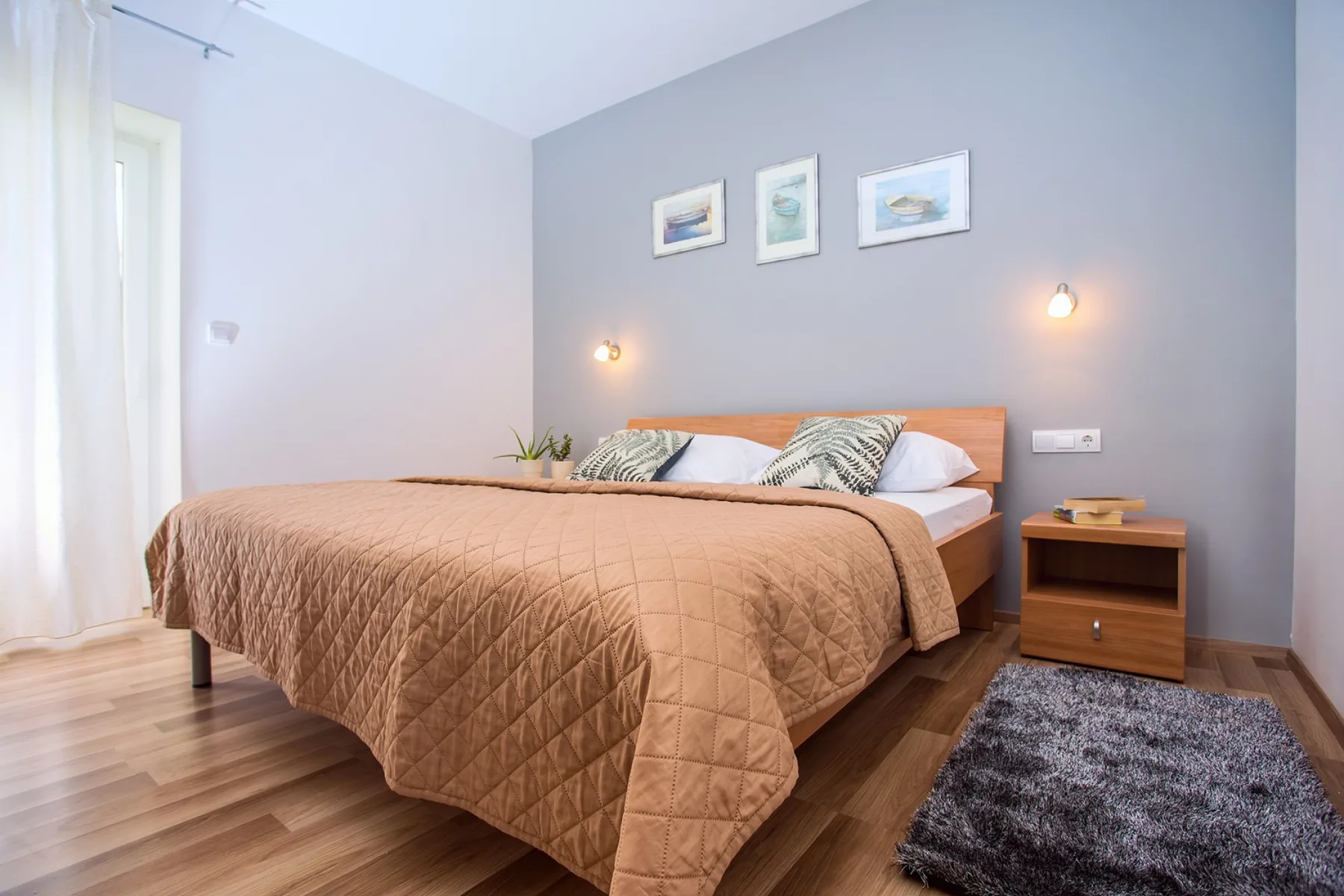 Un dormitorio con una cama tendida, cuadros enmarcados y luces junto a la cama.