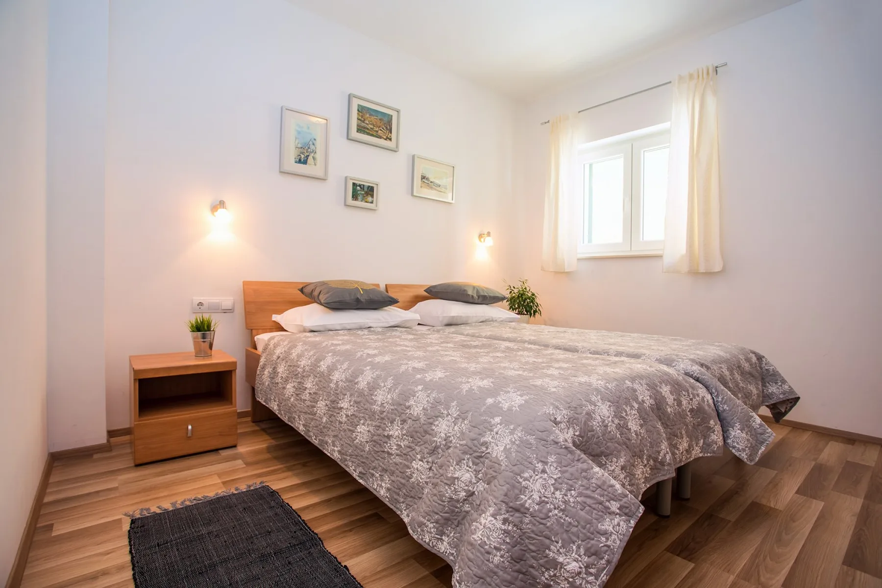 Un dormitorio con una cama, cuadros en la pared y una ventana con cortinas claras.