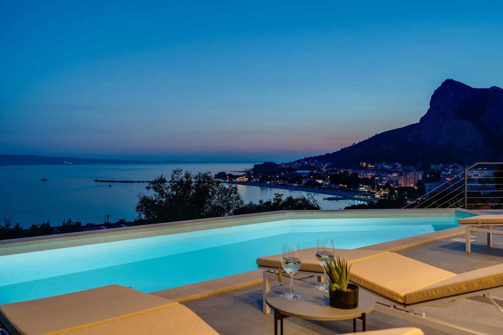 A poolside terrace overlooks a coastal bay at dusk.