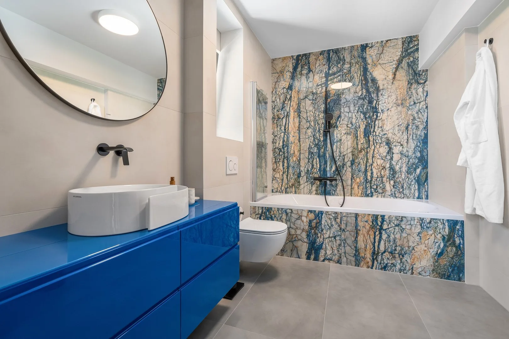 A modern bathroom with a blue vanity and a bathtub against a patterned wall.