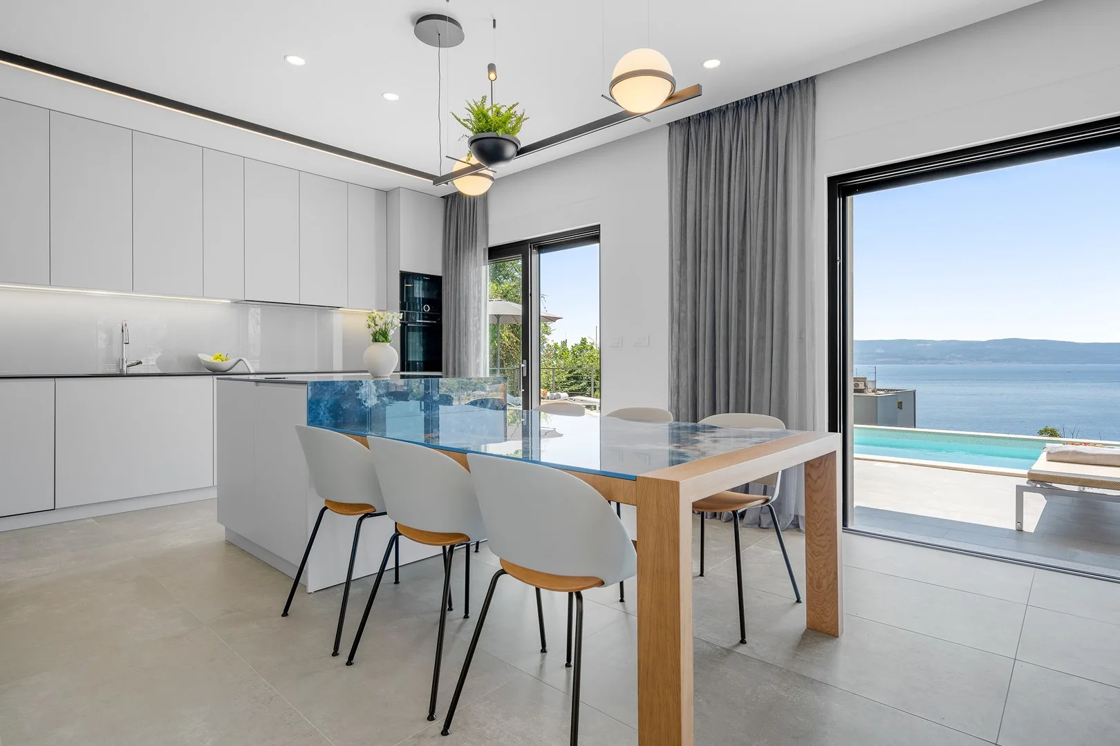 A modern kitchen and dining area opens onto a terrace overlooking the sea.