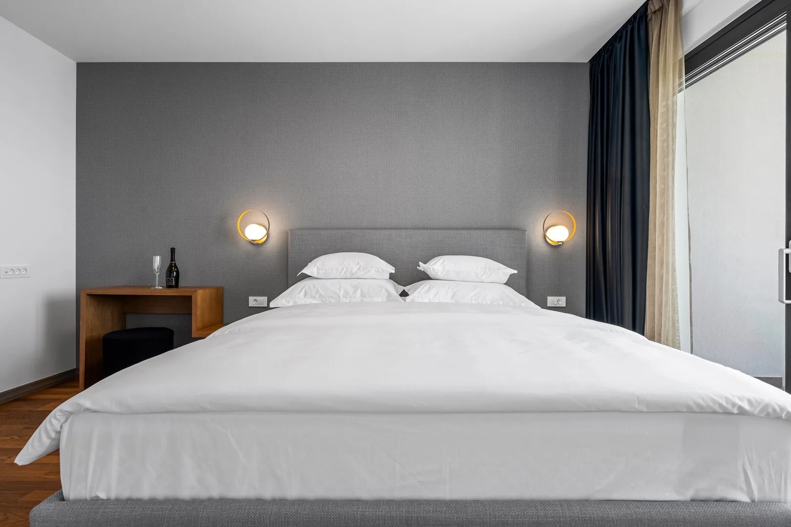 A bedroom with a neatly made bed, bedside lights, and a small desk.