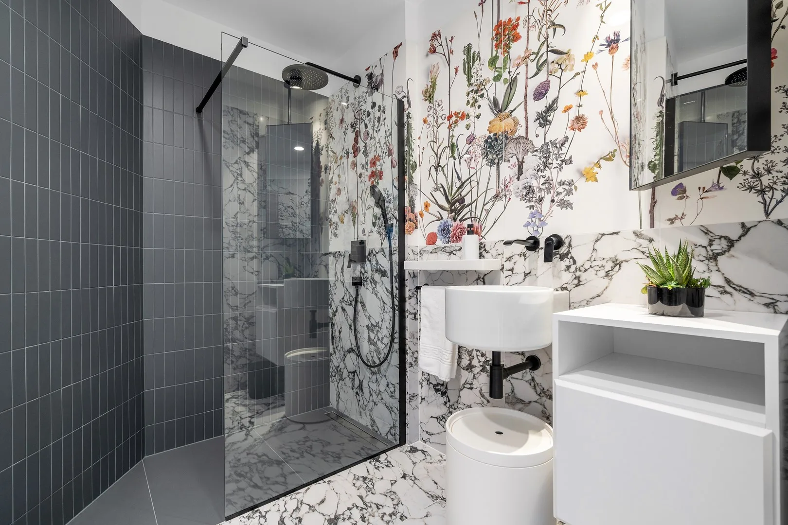 A bathroom with a glass shower, sink, and floral wall design.