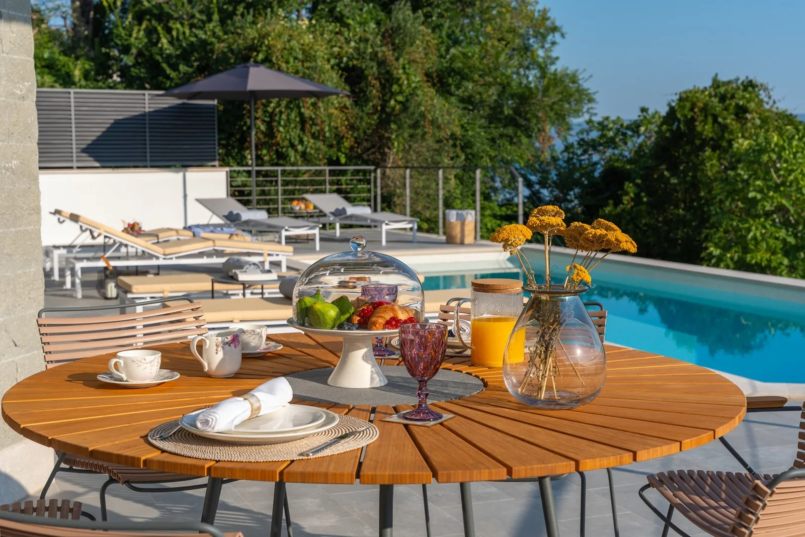 A poolside dining table is set with dishes beside a swimming pool.