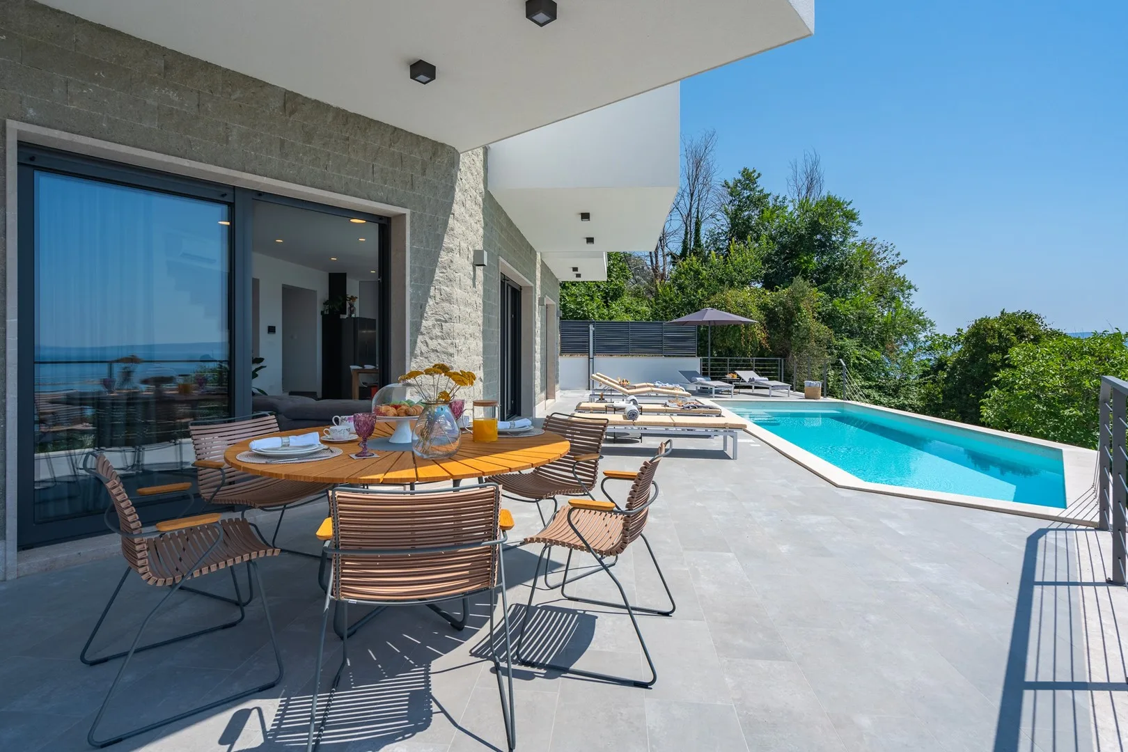 A sunny patio with outdoor seating beside a swimming pool.
