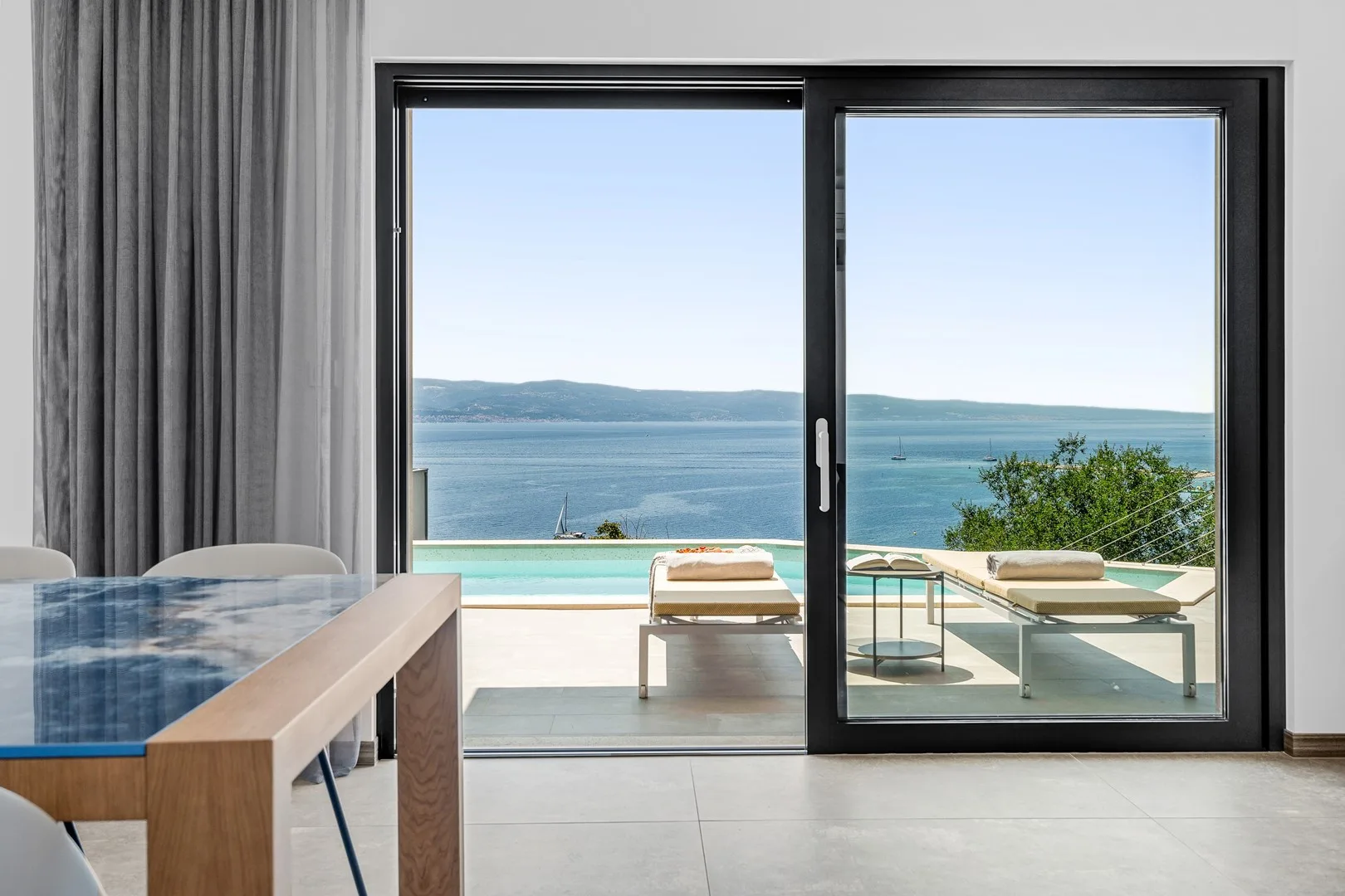 A dining area opens onto a terrace with a pool and views of the sea.