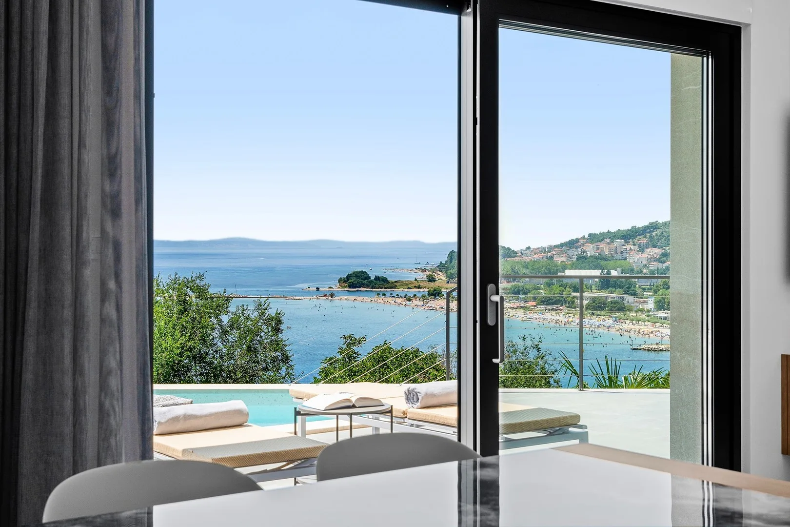 A bright room opens onto a terrace with a pool and views of the sea.