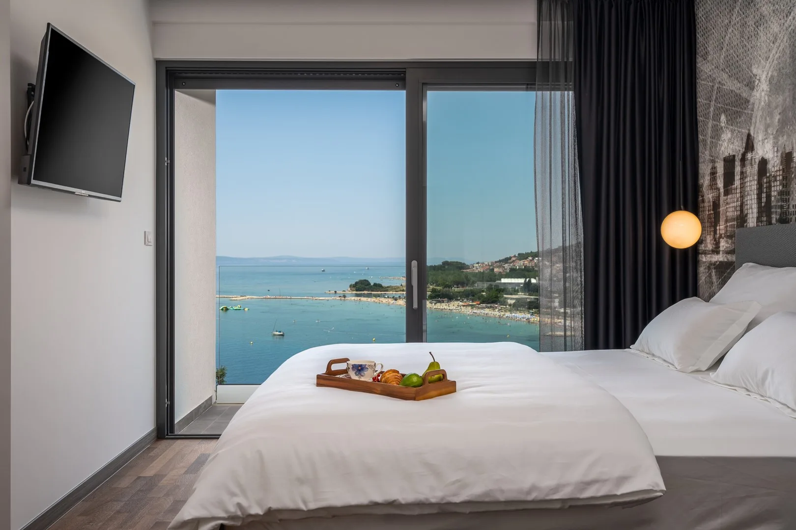 A bedroom with a neatly made bed and a view of the sea through glass doors.