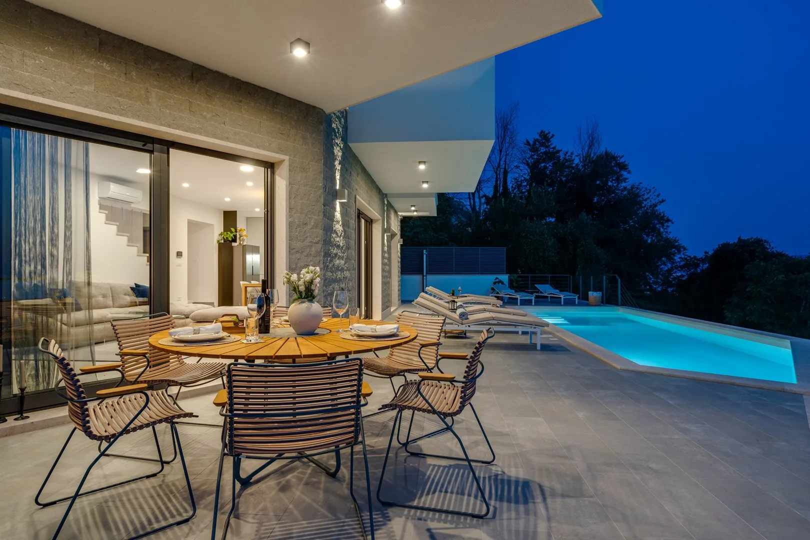A covered outdoor dining area overlooks a swimming pool beside a modern house.