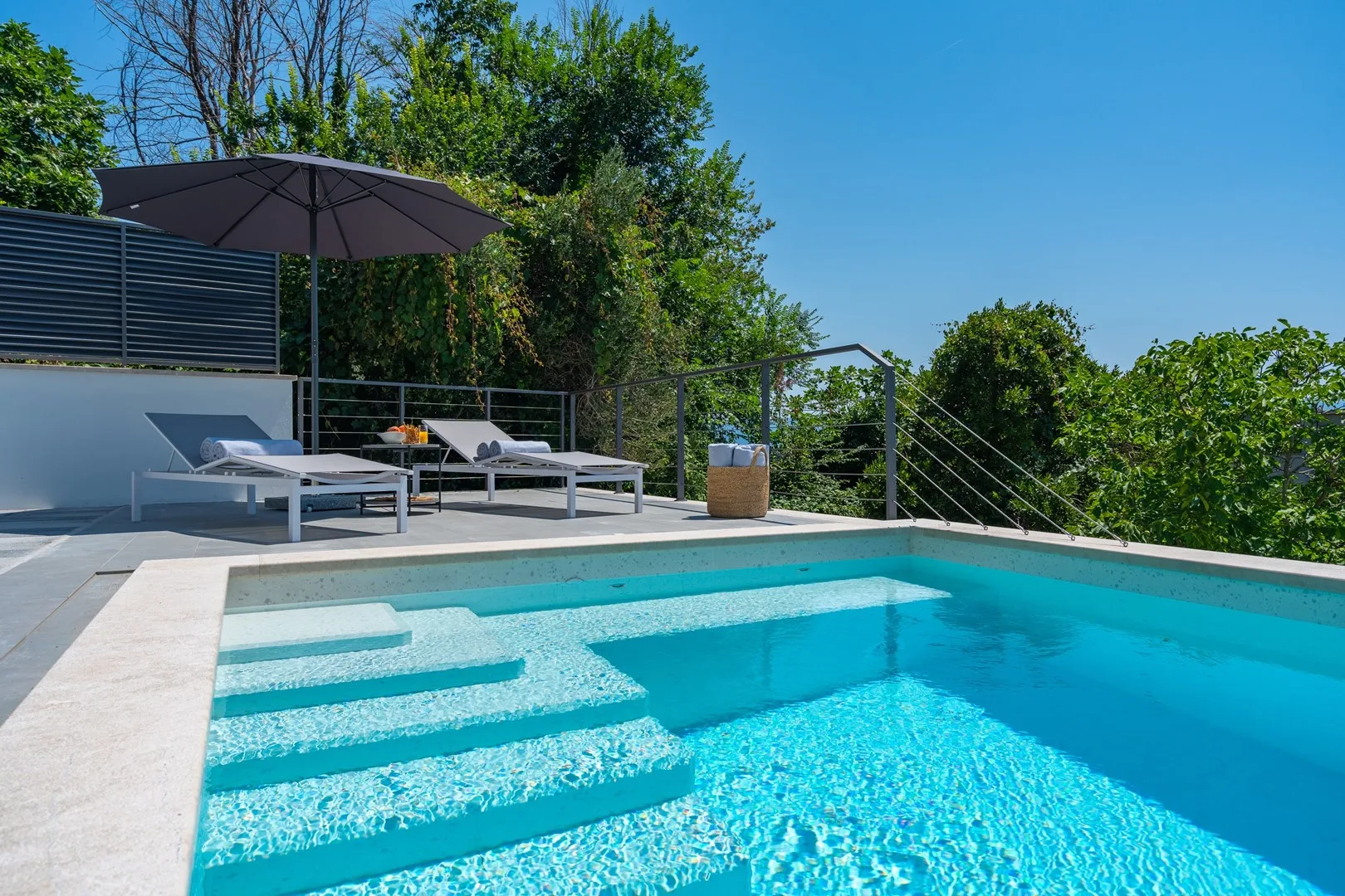 An outdoor swimming pool with lounge seating and an umbrella beside it.