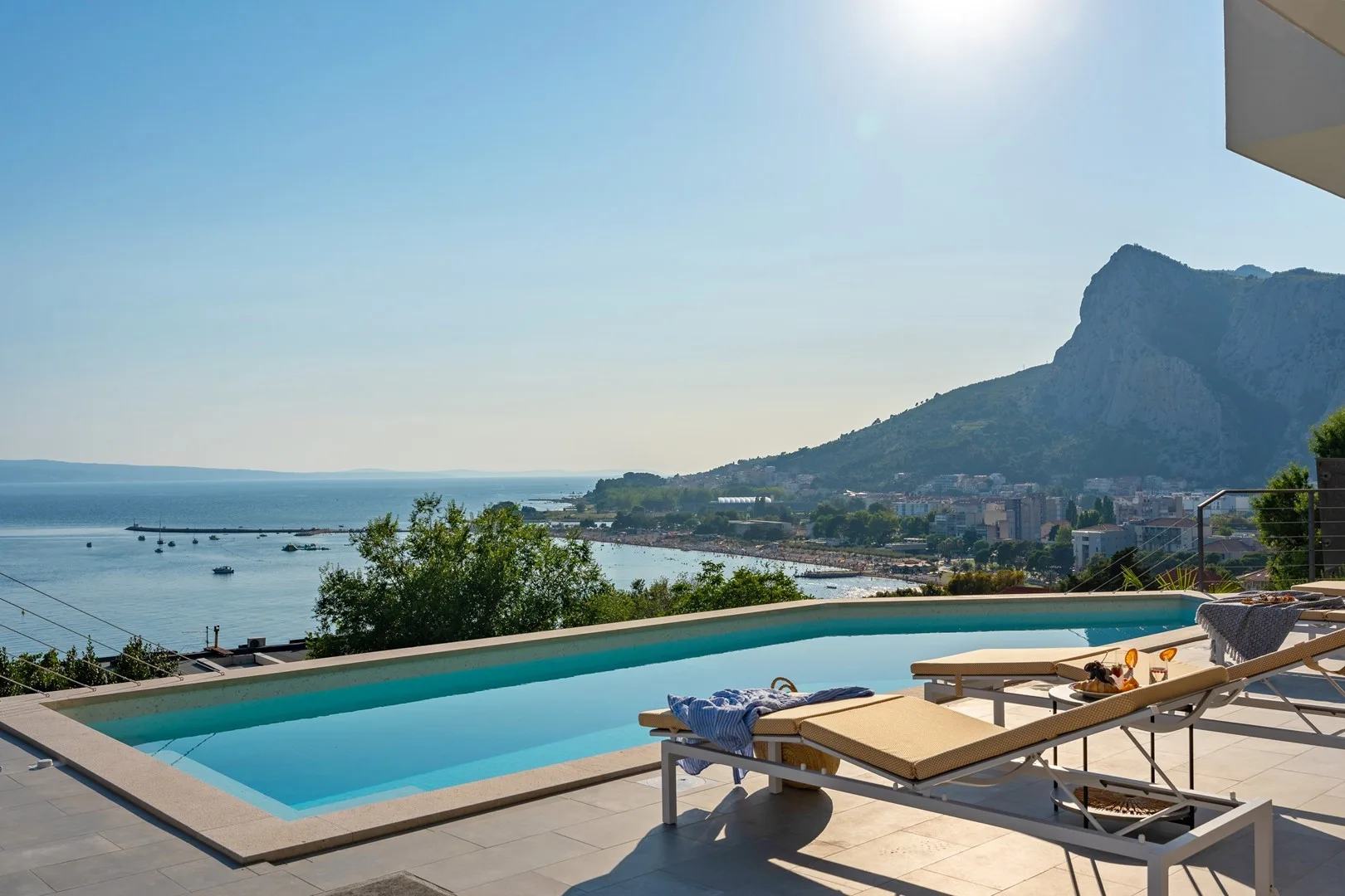 An outdoor swimming pool overlooks the sea and a mountain.