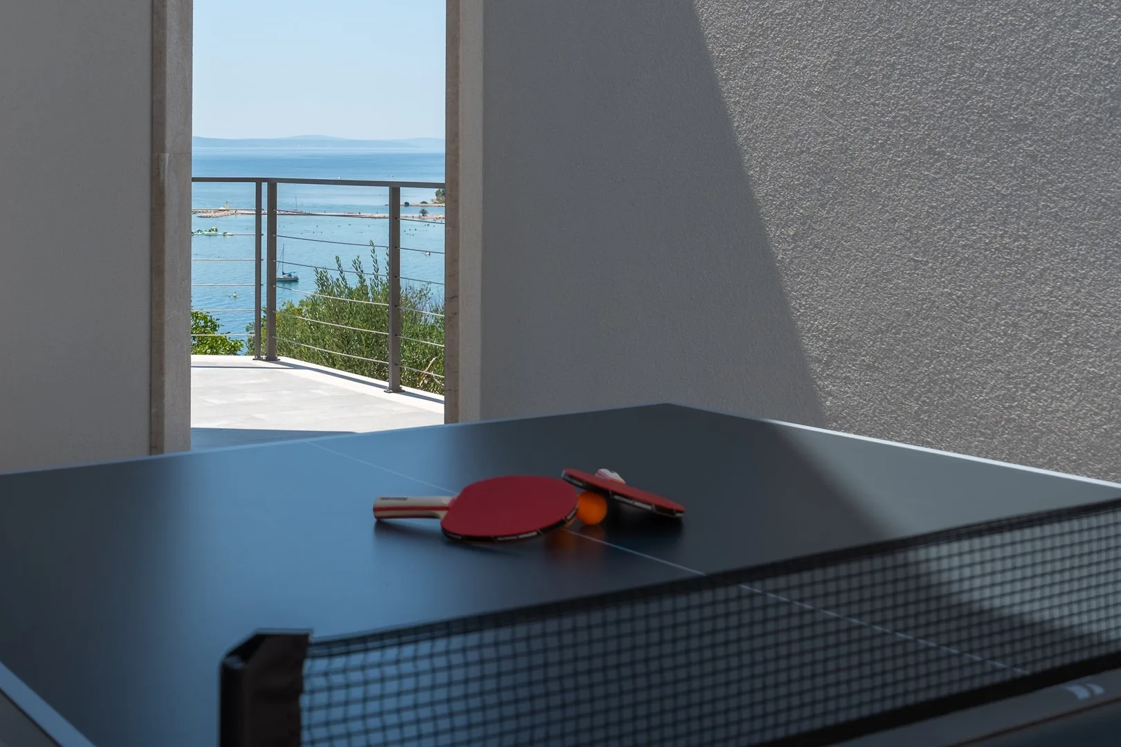 A ping-pong table with paddles sits beside an open view of the sea.