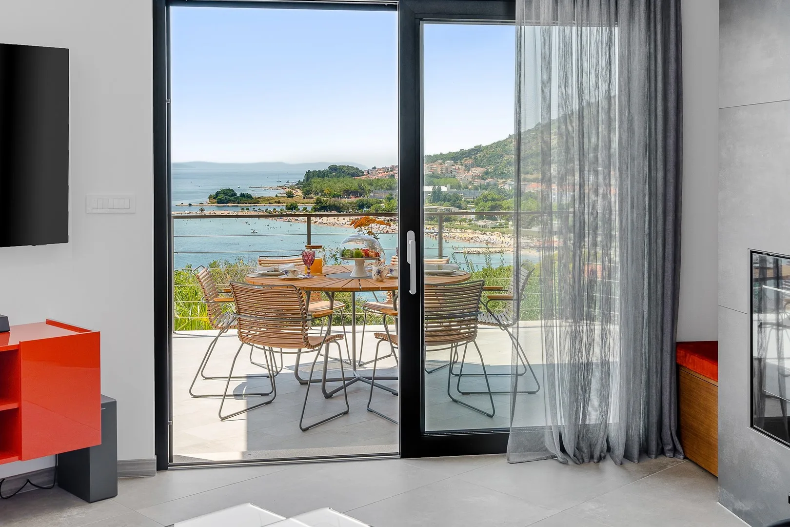 A glass door opens onto a patio with outdoor seating and a view of the water.
