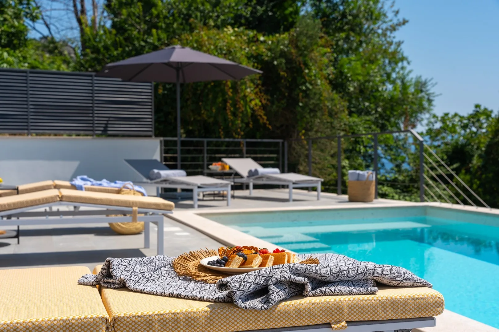 An outdoor swimming pool beside lounge seating and a shaded patio.