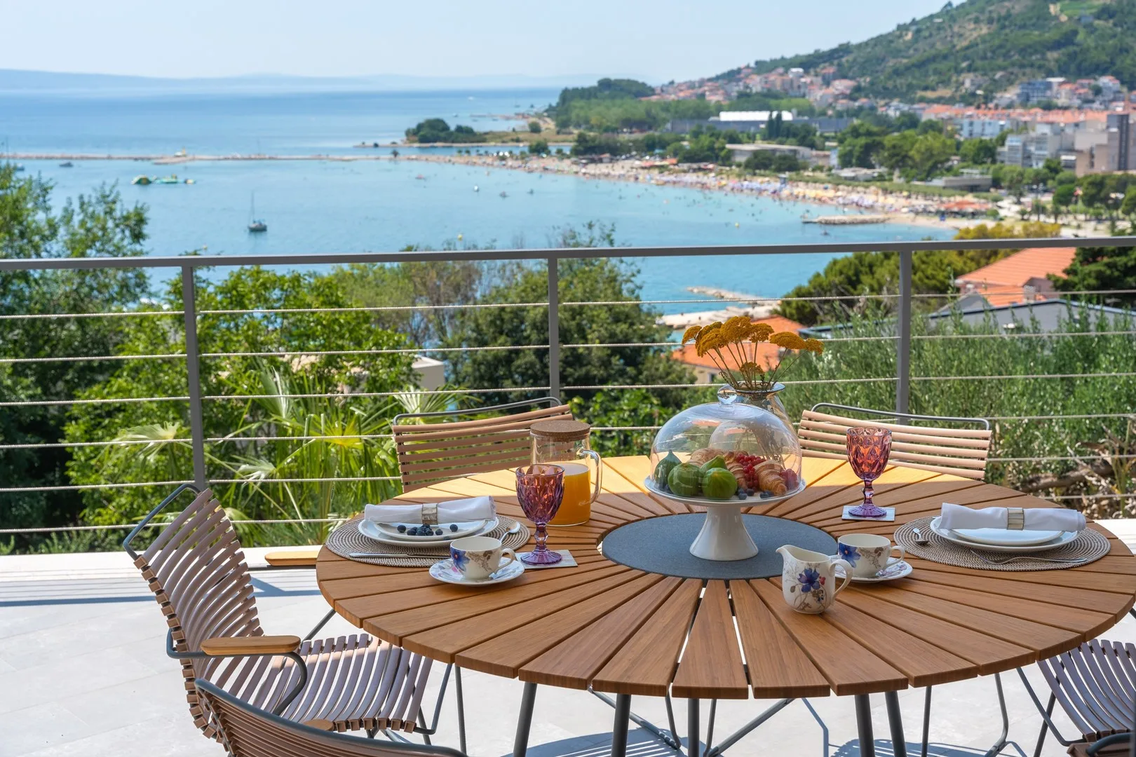 A seaside terrace dining area overlooks the bay, with a round table set for a meal.
