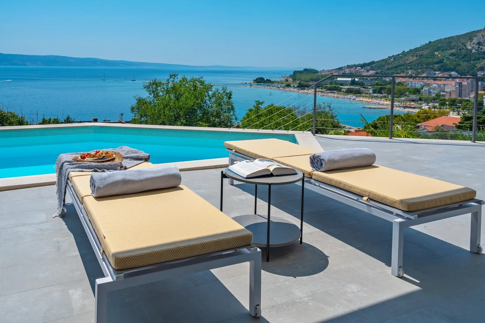 Poolside loungers sit beside a swimming pool overlooking the bay.