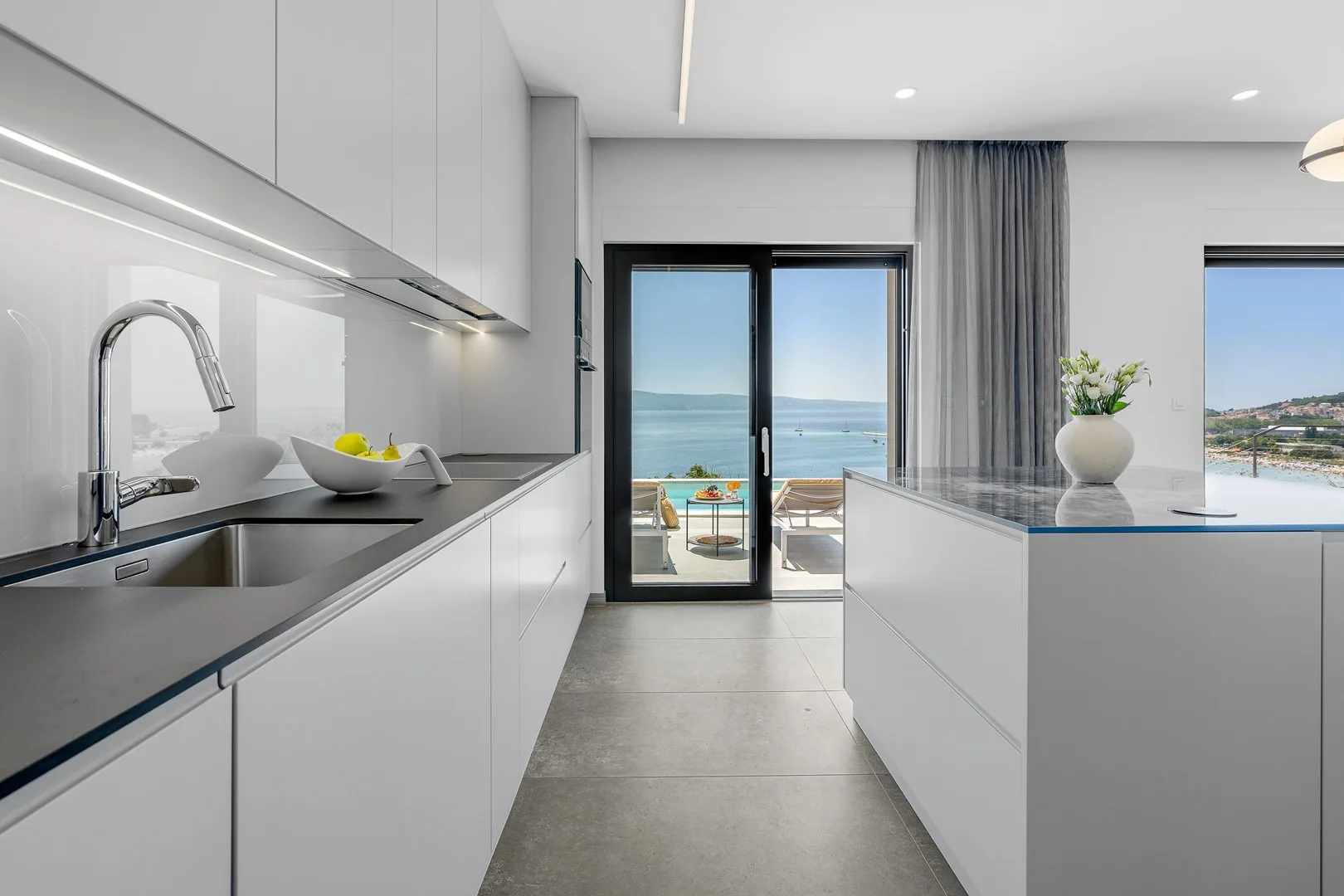 A modern kitchen opens toward a balcony with views of the sea.