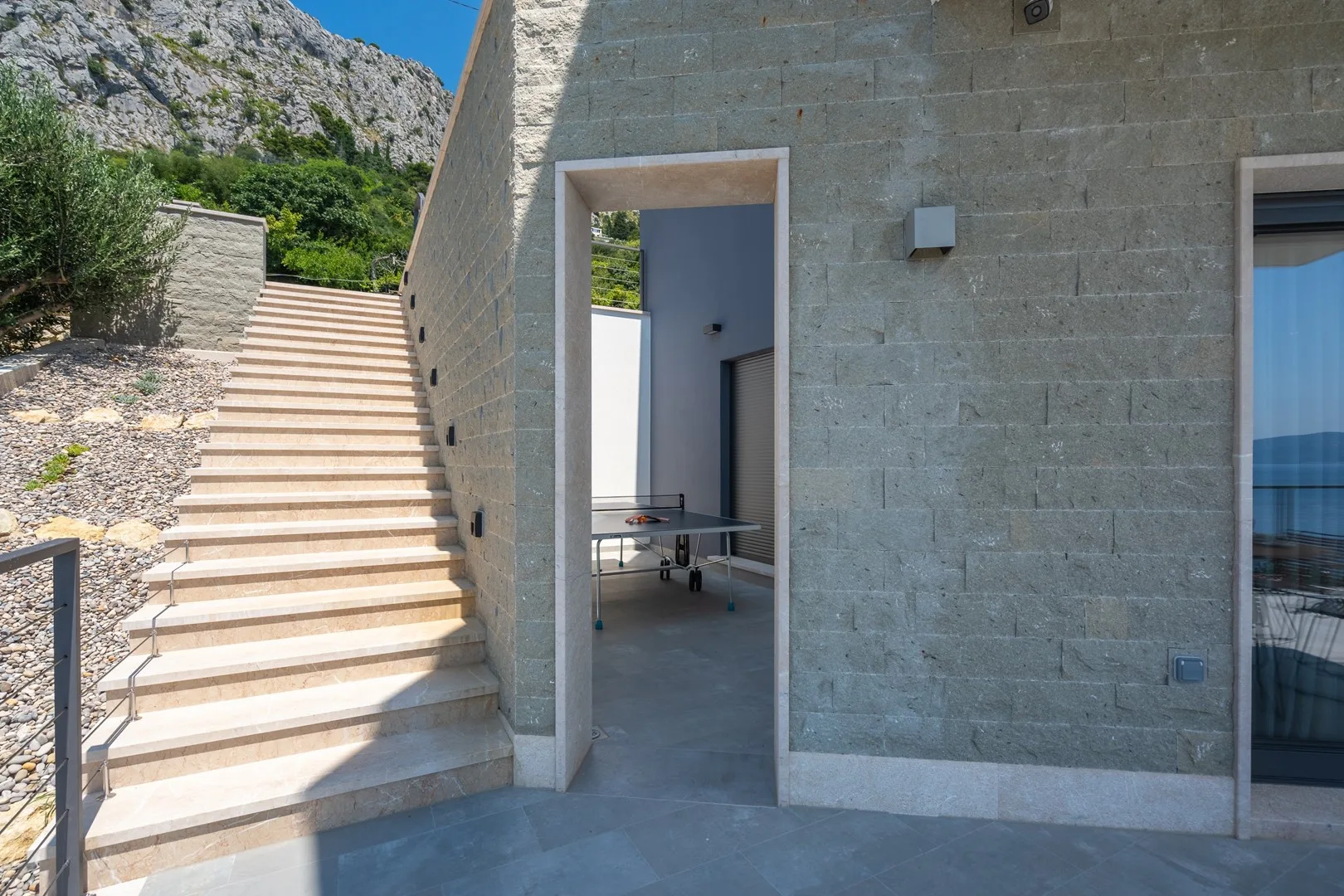 Exterior stone steps lead to an open doorway beside a stone wall.