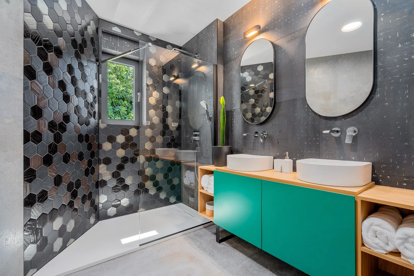 A modern bathroom with a glass shower, green vanity, and two sinks.