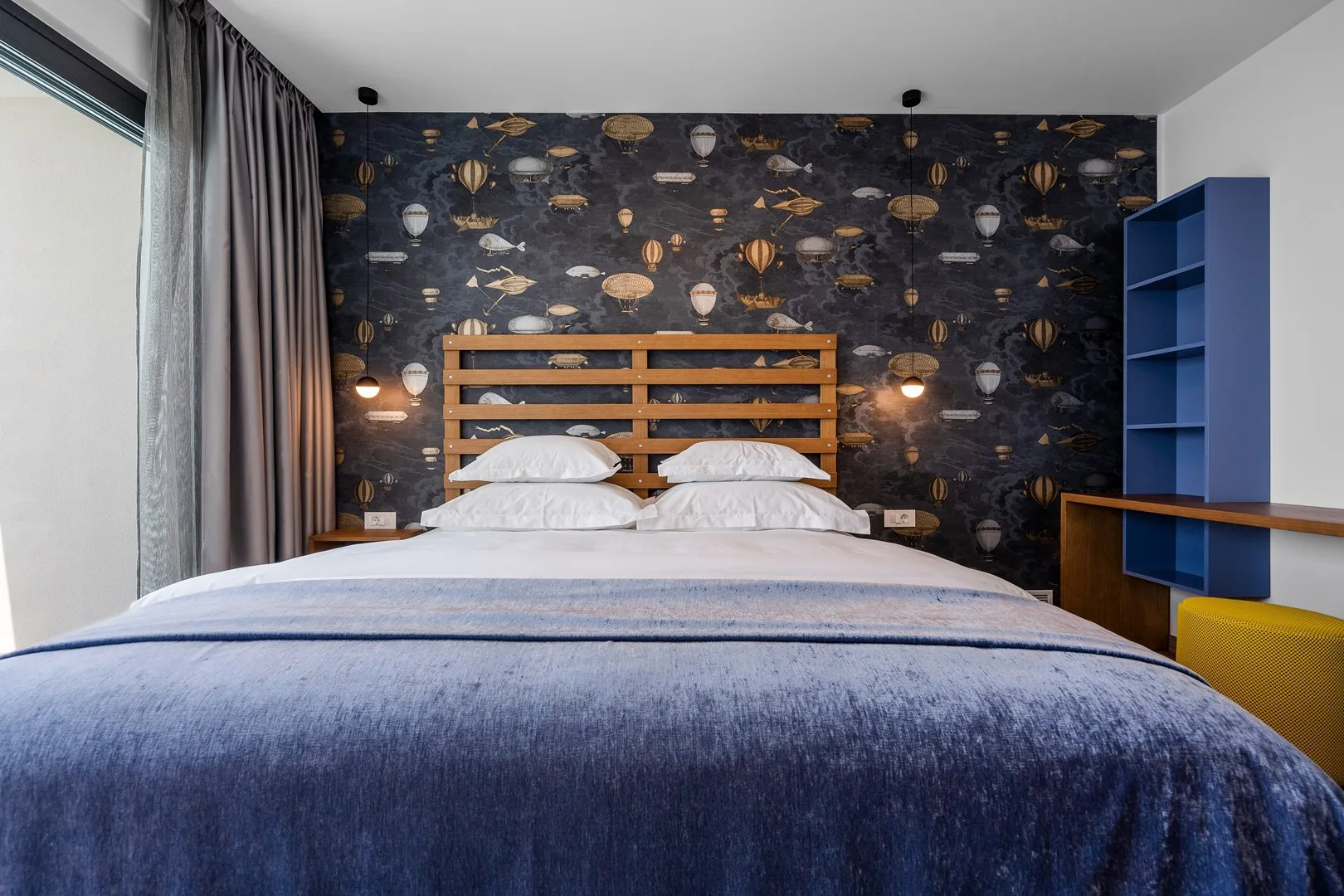 A bedroom with a bed, patterned wallpaper, and blue shelving.