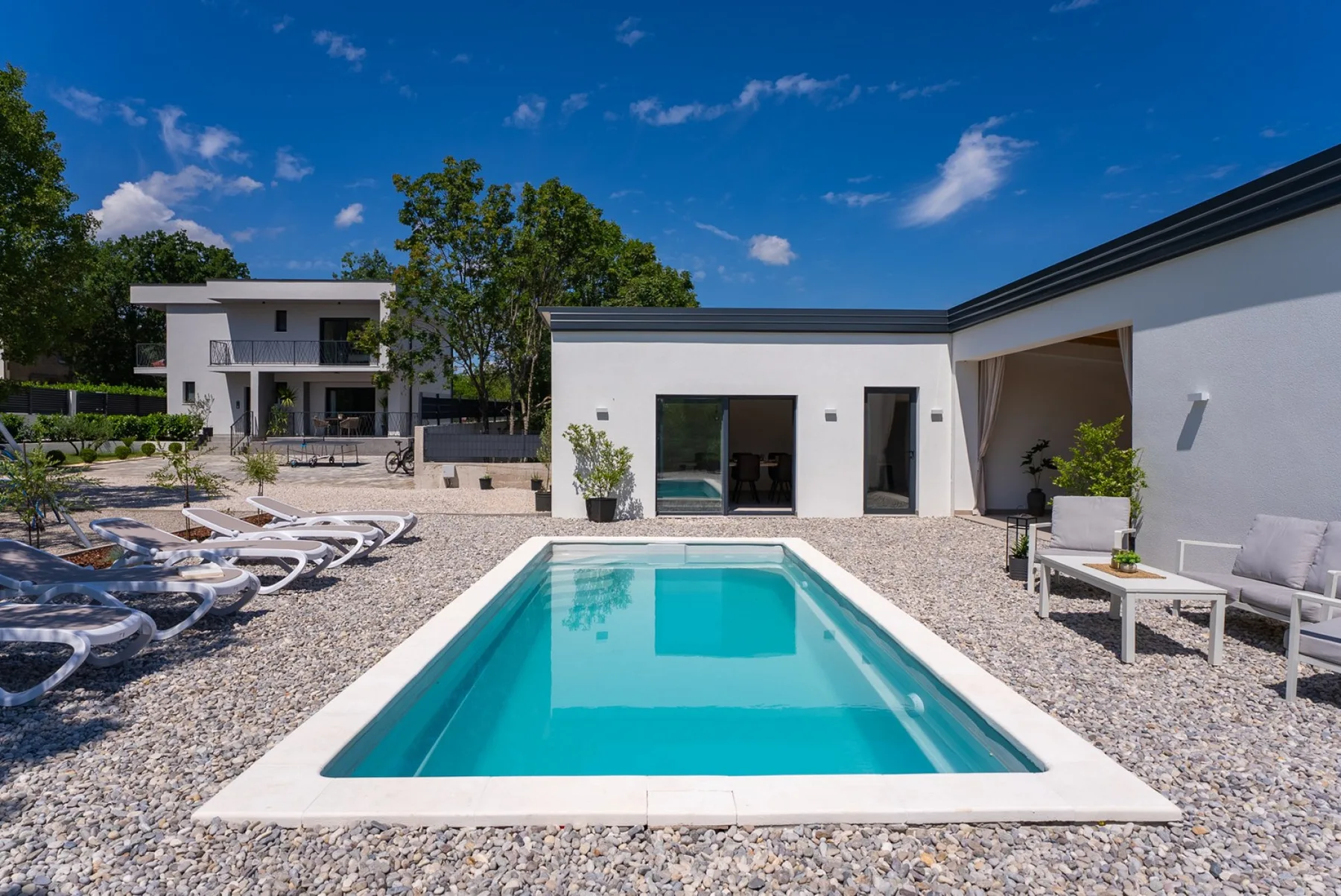 An outdoor swimming pool sits in a gravel courtyard beside a modern white building.