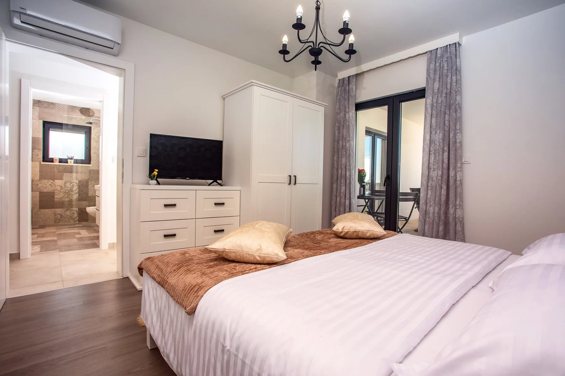A bedroom with a bed, a television, and a wardrobe beside curtained glass doors.