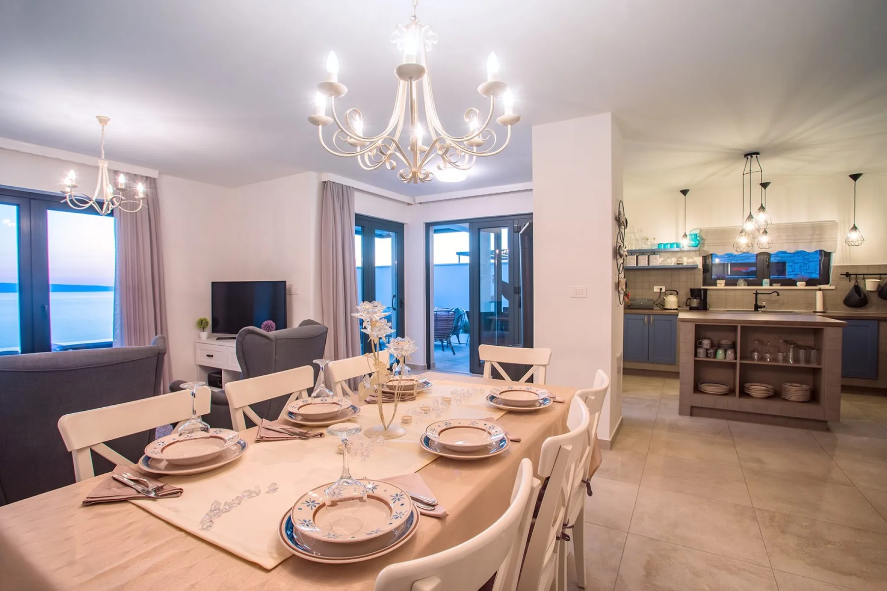 A dining area with a set table opens onto a kitchen.