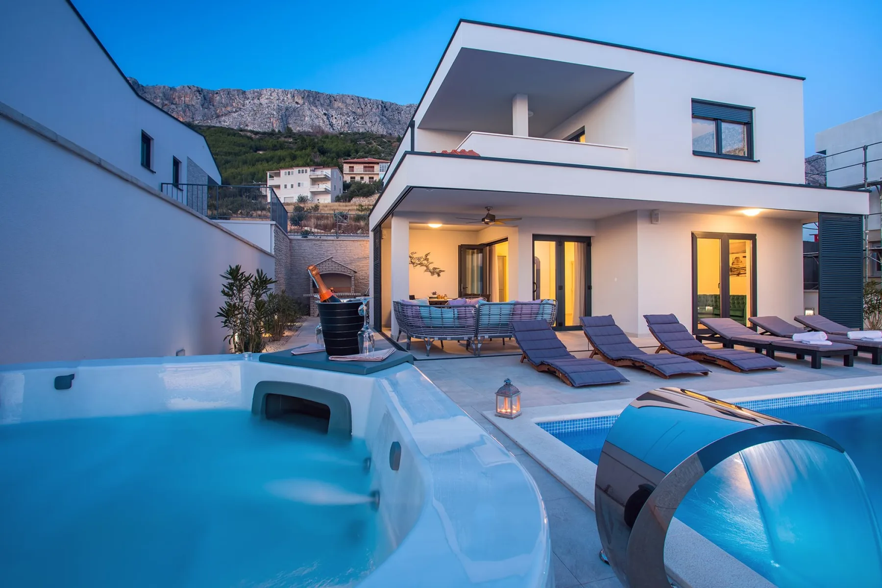 A modern house faces a swimming pool and lounge chairs at dusk.