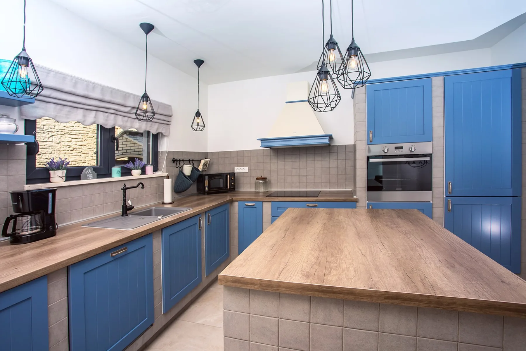 A blue-and-wood kitchen with a large central island and pendant lights.