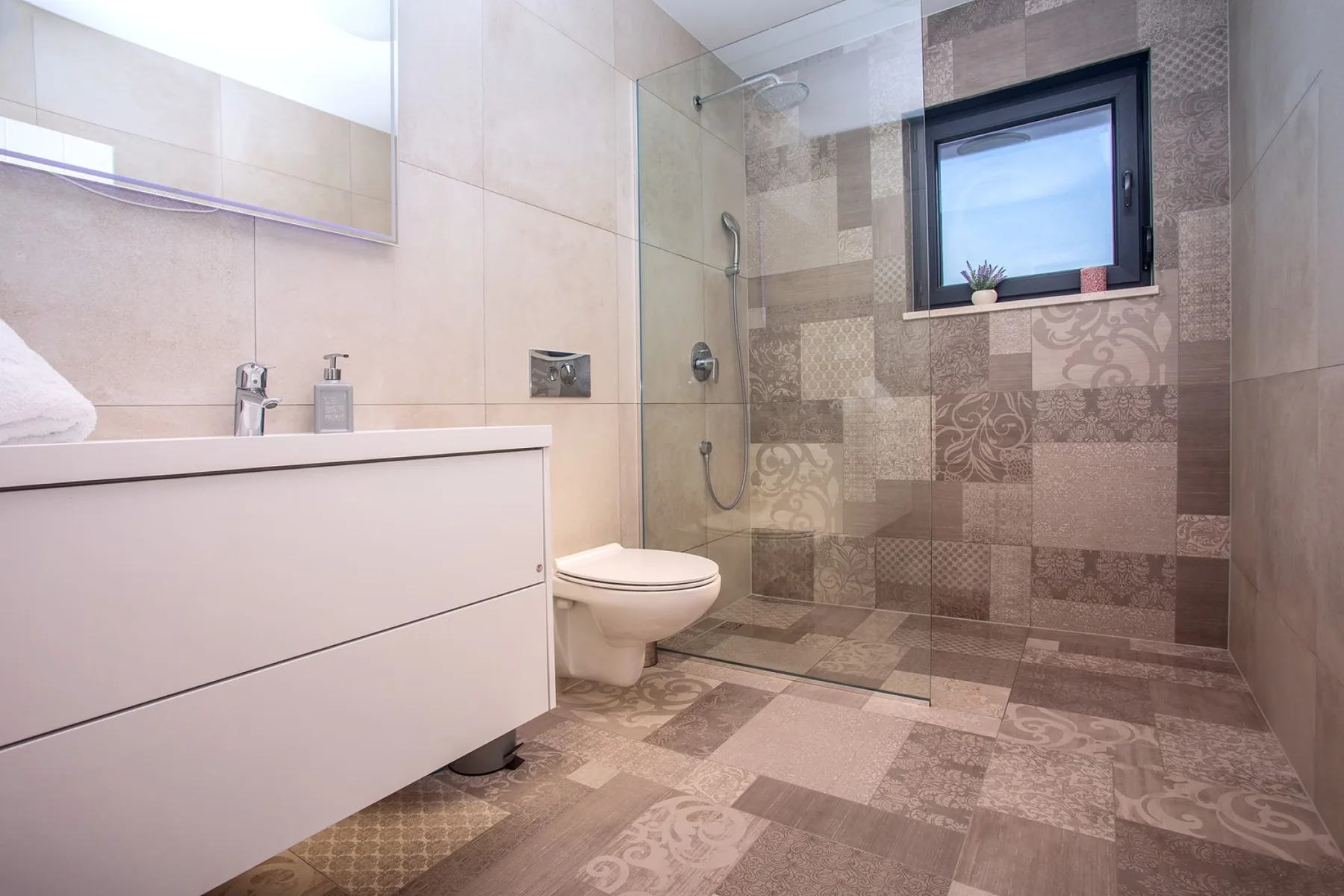 A tiled bathroom with a vanity, toilet, and glass shower.