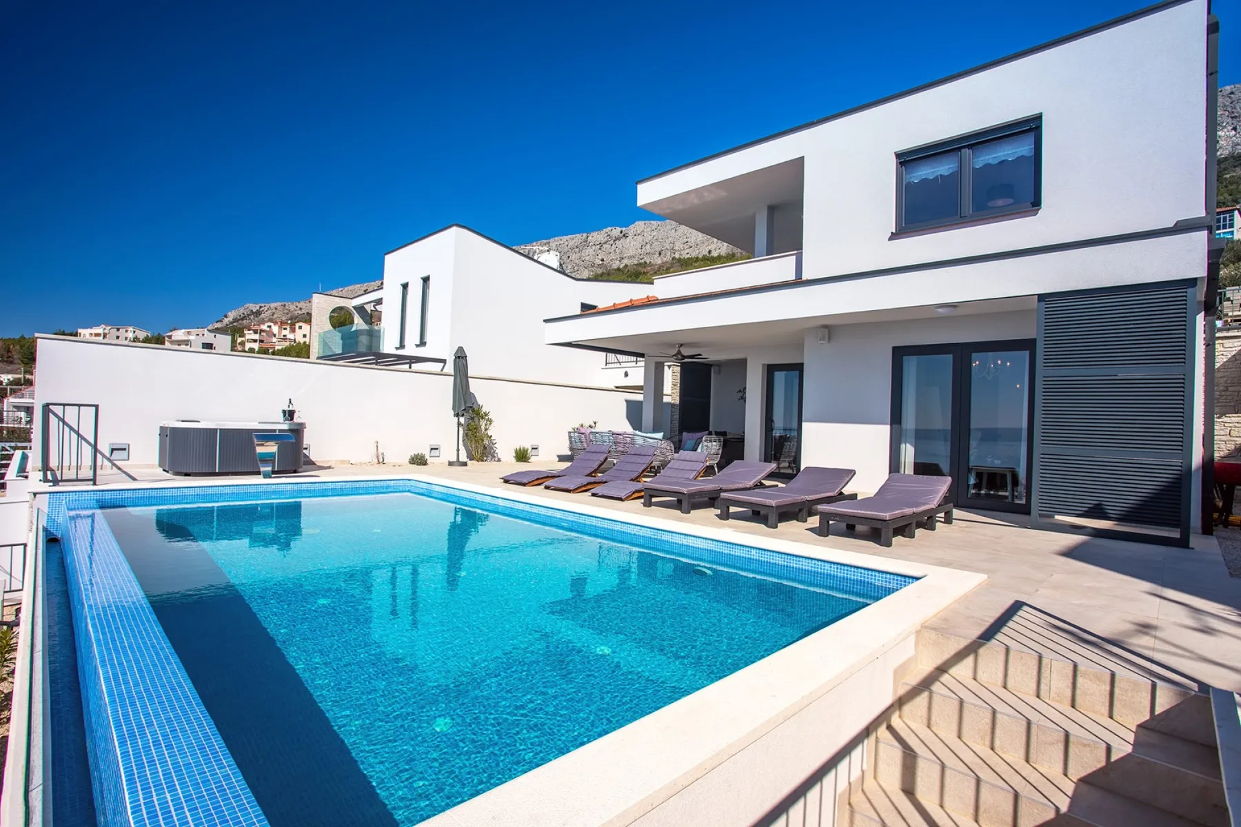 A modern house overlooks a swimming pool with lounge seating on the patio.