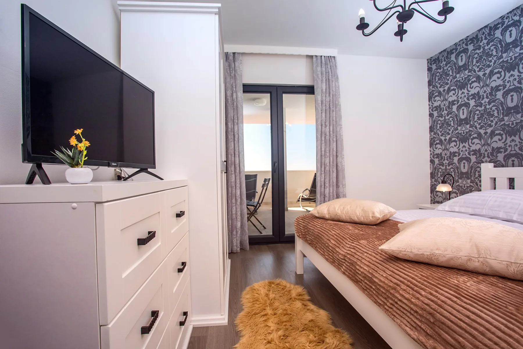 A bedroom with twin beds, a television, and glass doors opening onto a balcony.