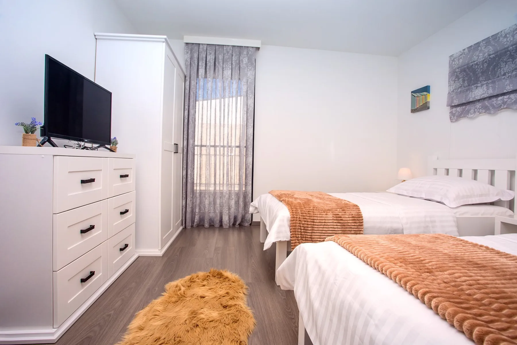 A bright bedroom with two beds, a dresser, and a television.