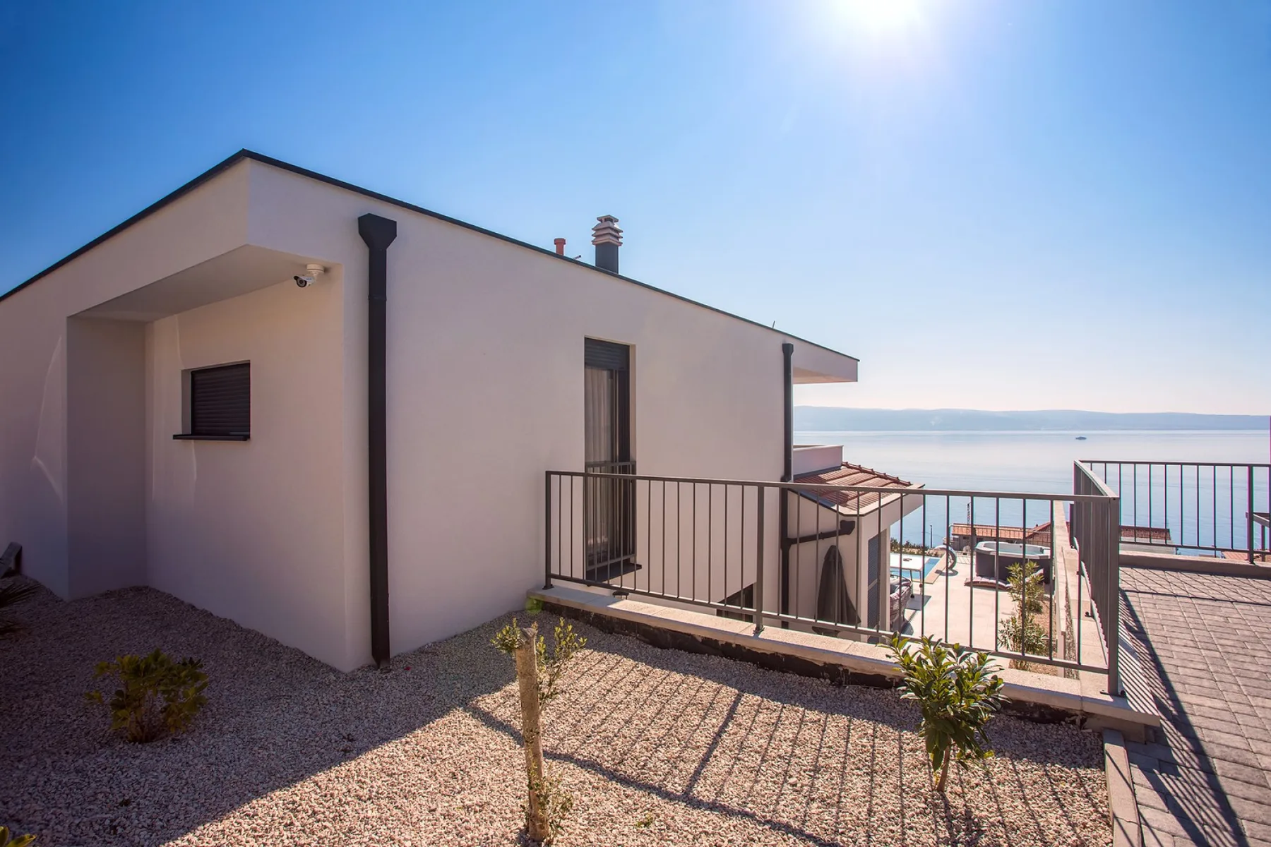 A modern house opens onto a terrace overlooking the water.